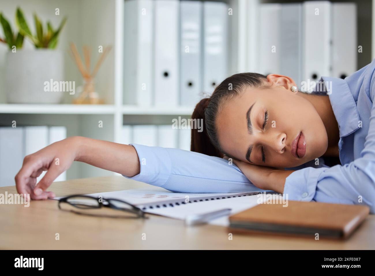 Tired, sleep and woman in business on her table feeling burnout and overworked while sleeping in her office. Nap, dreaming and exhausted with fatigue Stock Photo