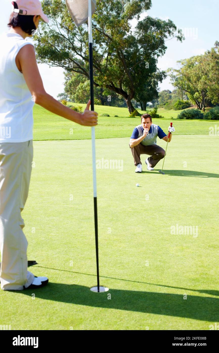 Man preparing to putt. Couple playing golf with man preparing to putt the ball. Stock Photo