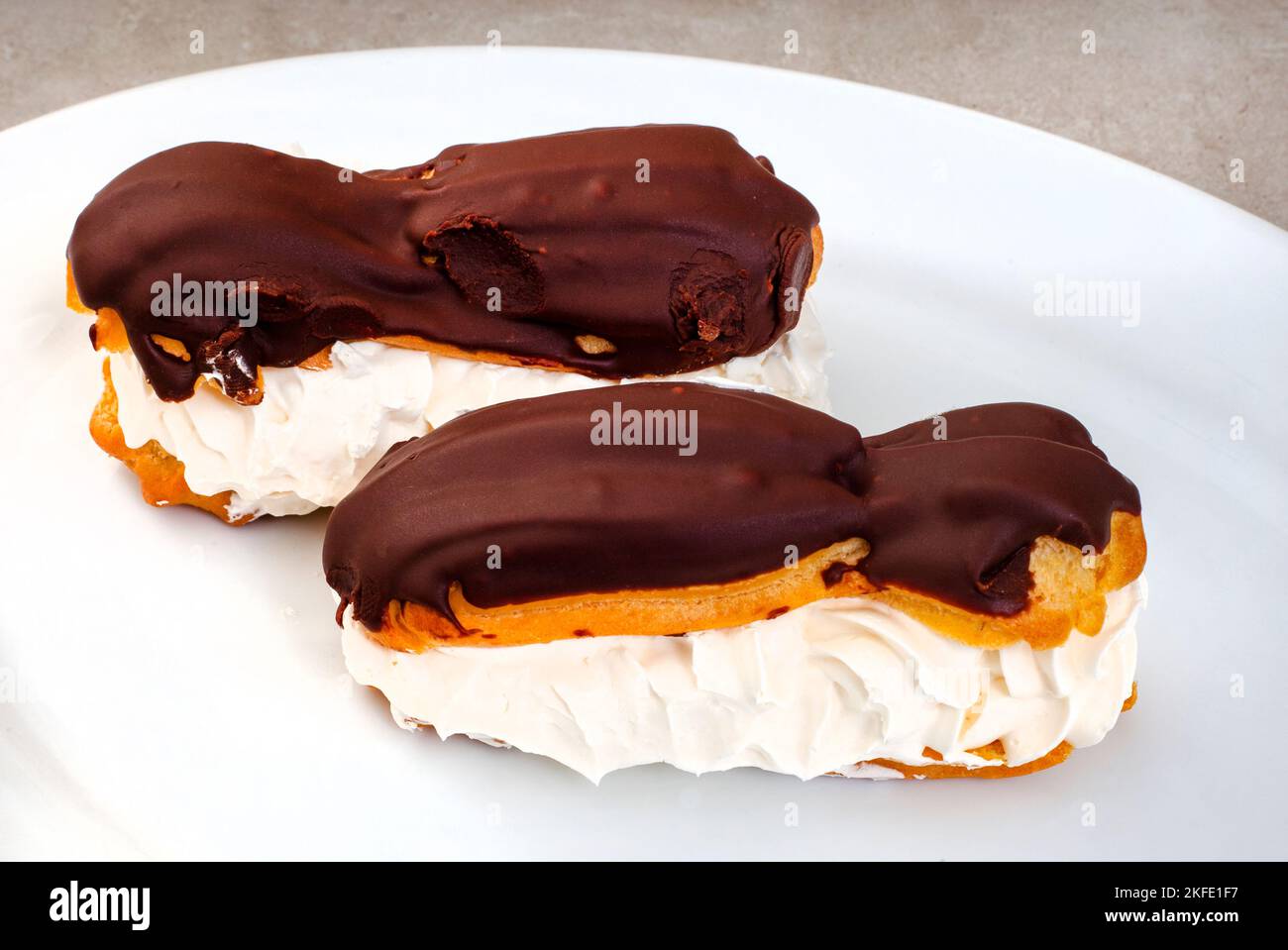 two freshly made chocolate eclairs on white plate with copy space Stock Photo