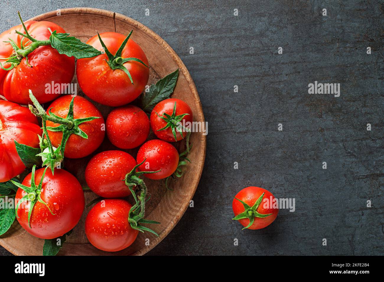 Fresh tomatoes in a plate on a dark background. Harvesting tomatoes. Top view Stock Photo