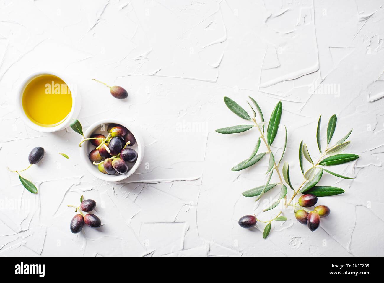 Olive oil in bowl with fresh olives fruit and olive branch on white background Stock Photo