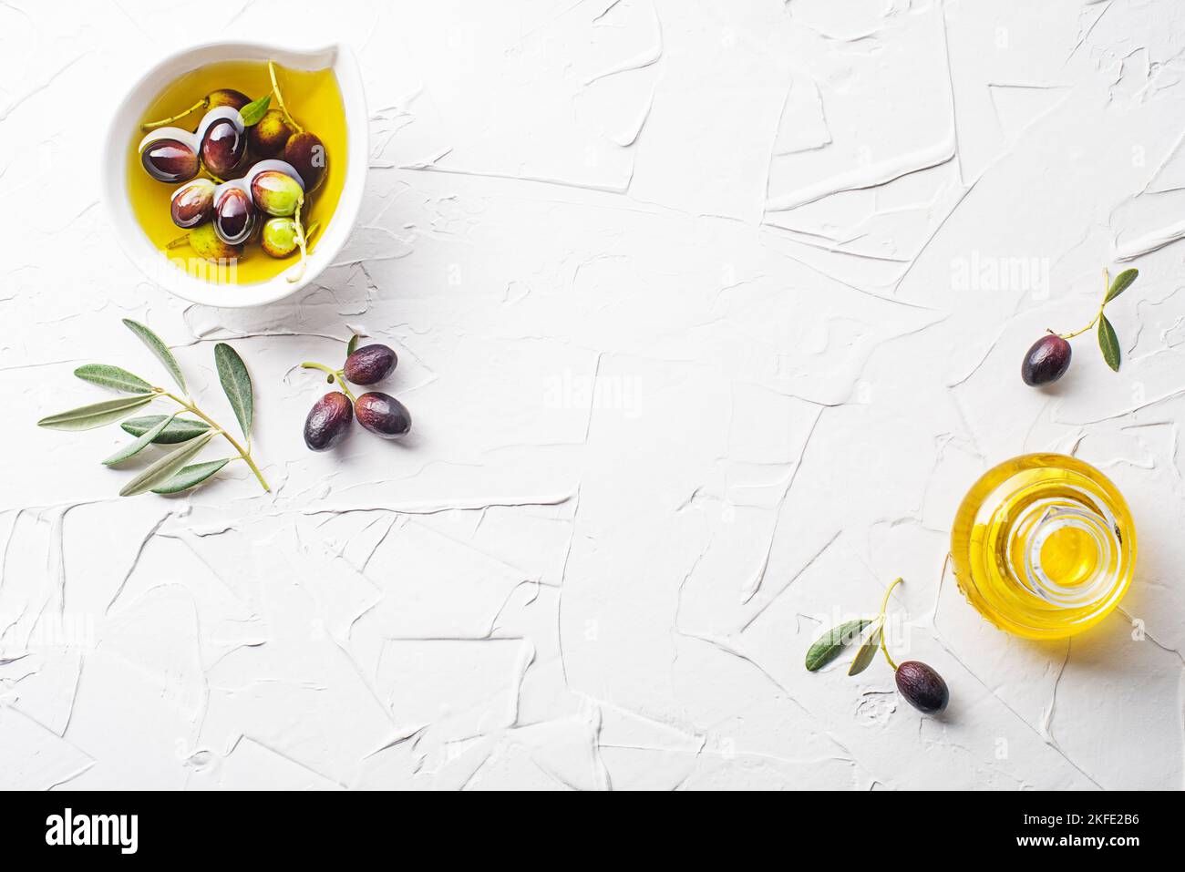 Olive oil in bowl and bottle with fresh olives fruit and olive branch on white background Stock Photo