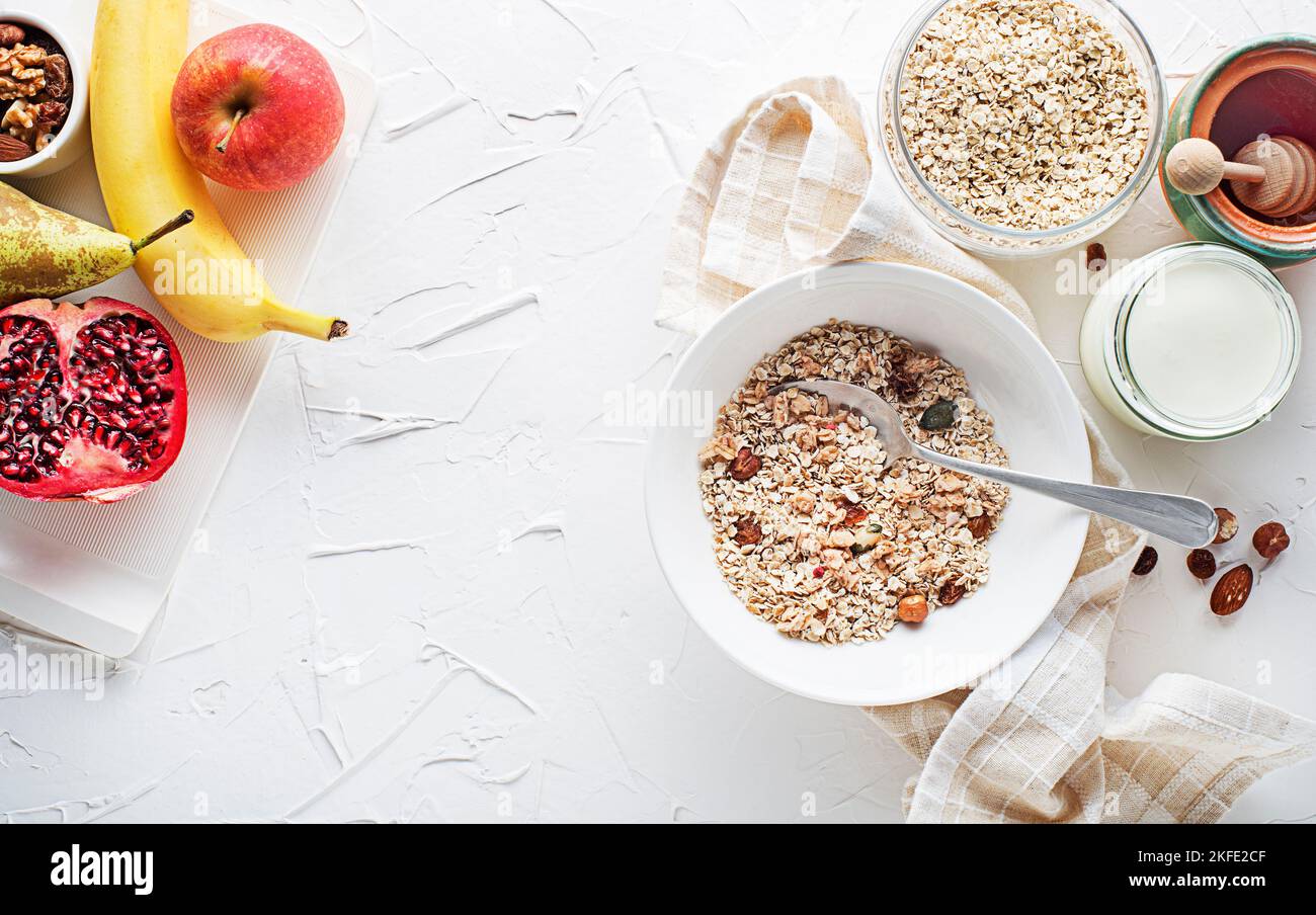 A bowl of dry granola and muesli served with fresh fruit, nuts and honey. Oatmeal plate. Healthy food, diet. Top view. Stock Photo