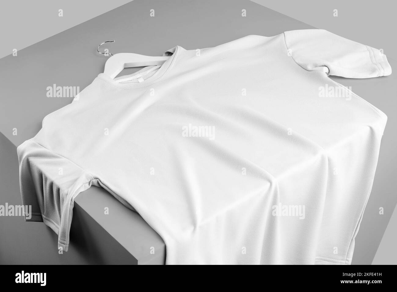 Mockup of an oversized white t-shirt, folded on top of a cube, front view, with space for design, pattern, advertising in an online store. Template bl Stock Photo