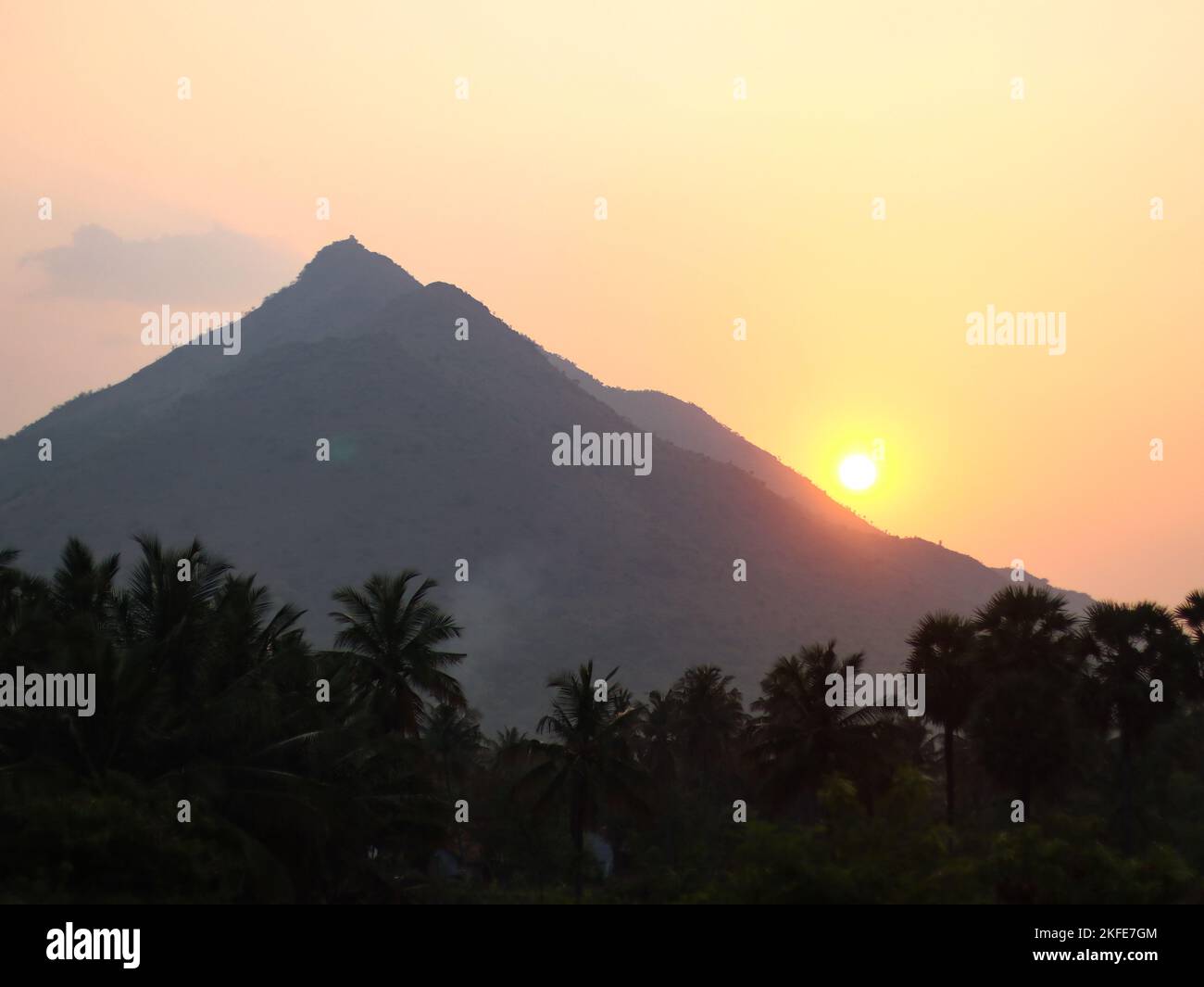 a phenomenal bright orange sunrise over the mountain above the forest trees during an early summer morning Stock Photo