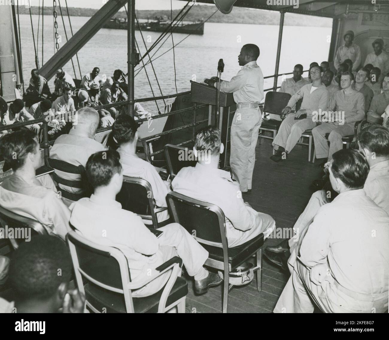 African American chaplain standing at the podium and conducting the religious service on deck of a U. S. Coast Guard vessel, South Pacific, 1939 - 1945. Stock Photo