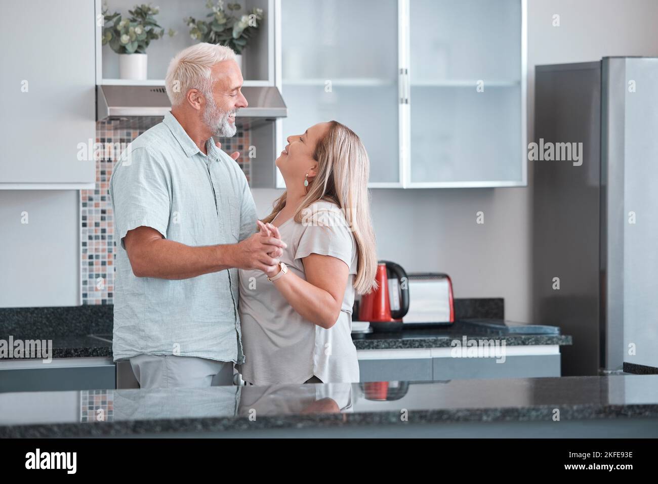 Love, dance and a senior couple in kitchen of home together enjoying weekend time and celebrate life with smile. Retirement, happiness and health, a Stock Photo