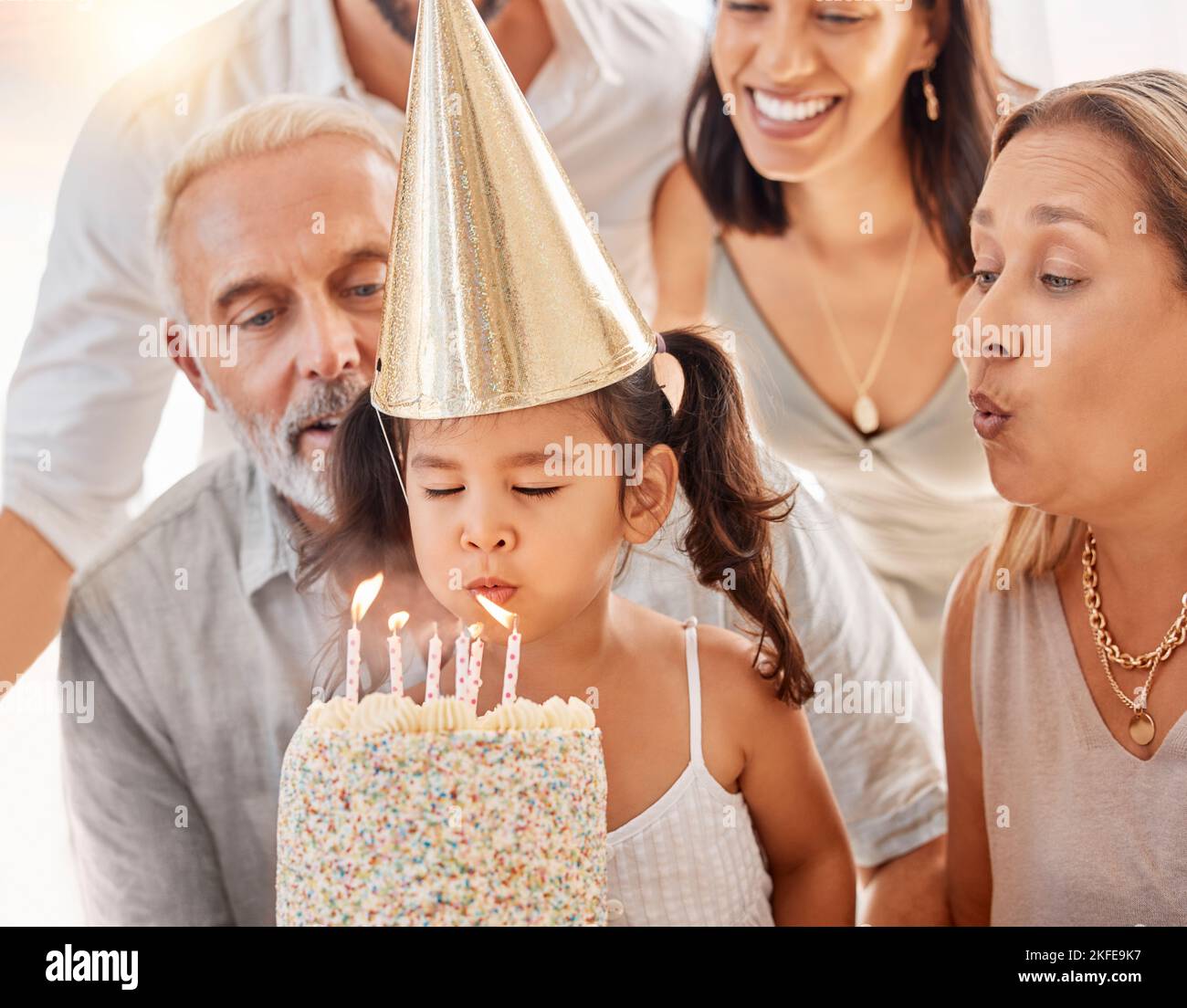 Blowing candles, birthday cake and happy family with a girl to celebrate with a wish, food and eating at a birthday party. Happy birthday, smile and Stock Photo