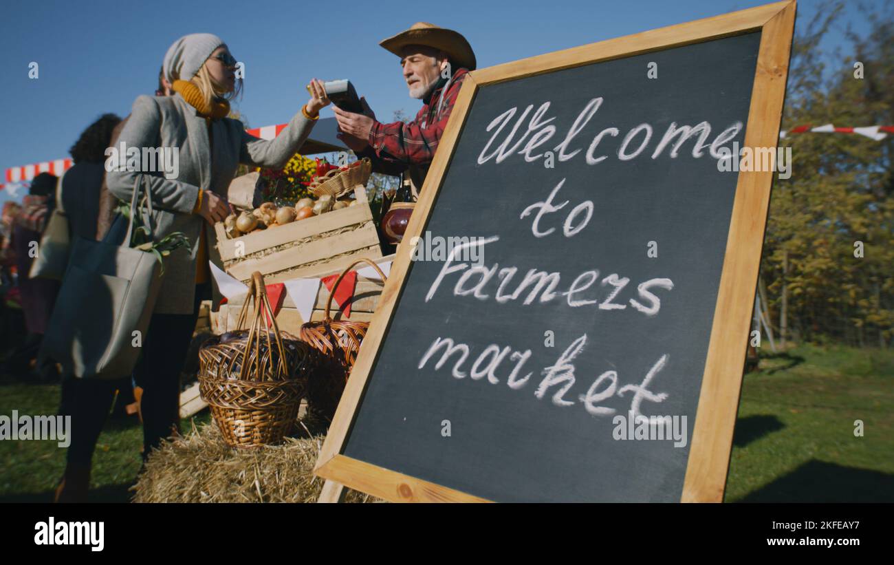 People shopping, choosing fruits and vegetables at local farmers market, packing goods in eco bags. Autumn fair on weekend outdoors. Vegetarian and organic food. Agriculture. Points of sale system. Stock Photo