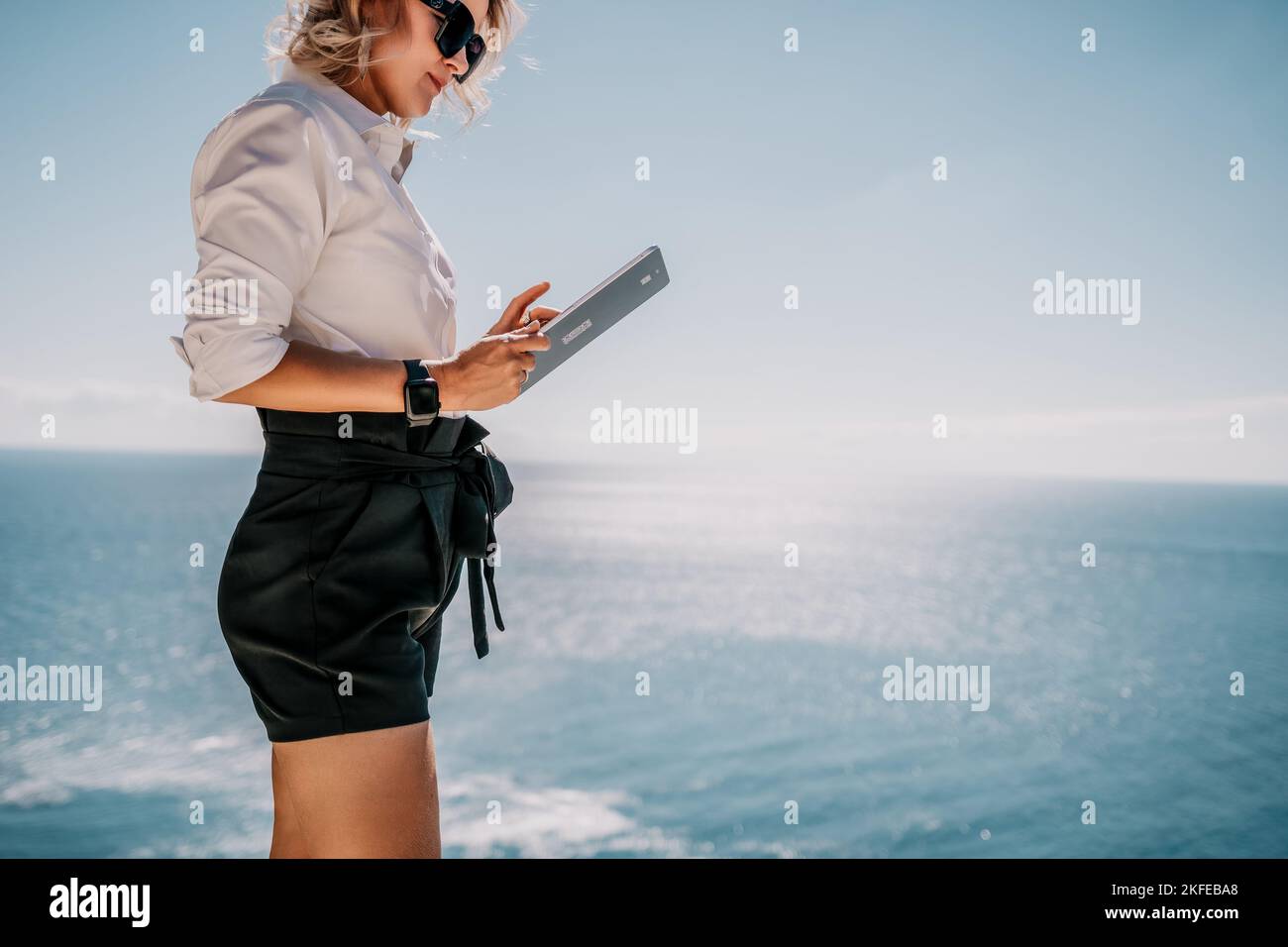 Digital nomad, Business woman working on tablet pc pad computer by the sea. Pretty lady with tablet pc on the sea, makes a business transaction online Stock Photo