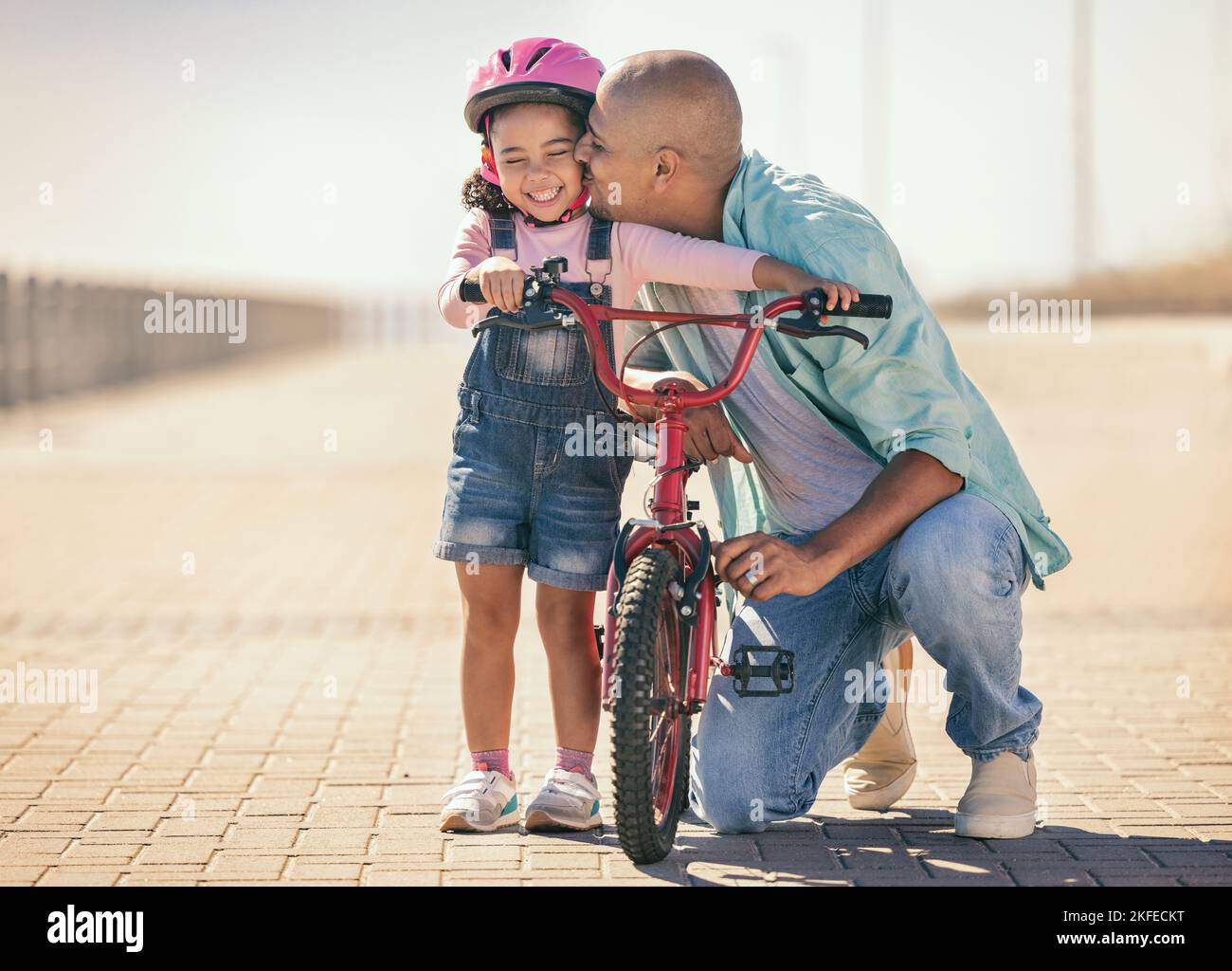 Father, child and kiss while outdoor with a bicycle with a girl learning, development and training on a bike in summer for fun, love and quality time Stock Photo