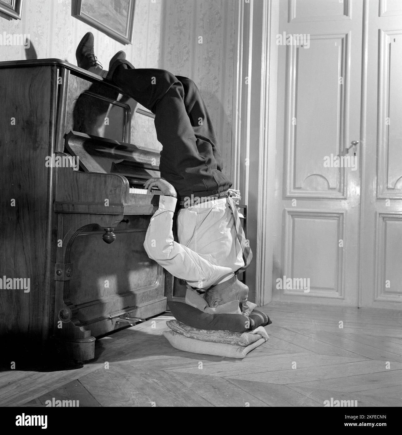 Man in the 1950s. With nothing else to do, this man finds that playing the piano standing upside down, works for him. Sweden 1957 Conard ref 3273 Stock Photo