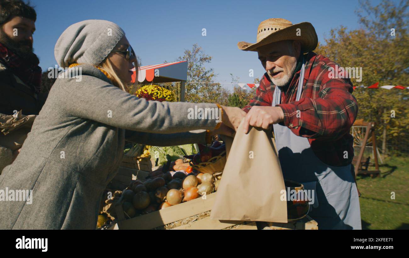 People shopping, choosing fruits and vegetables at local farmers market, packing goods in eco bags. Autumn fair on weekend outdoors. Vegetarian and organic food. Agriculture. Points of sale system. Stock Photo