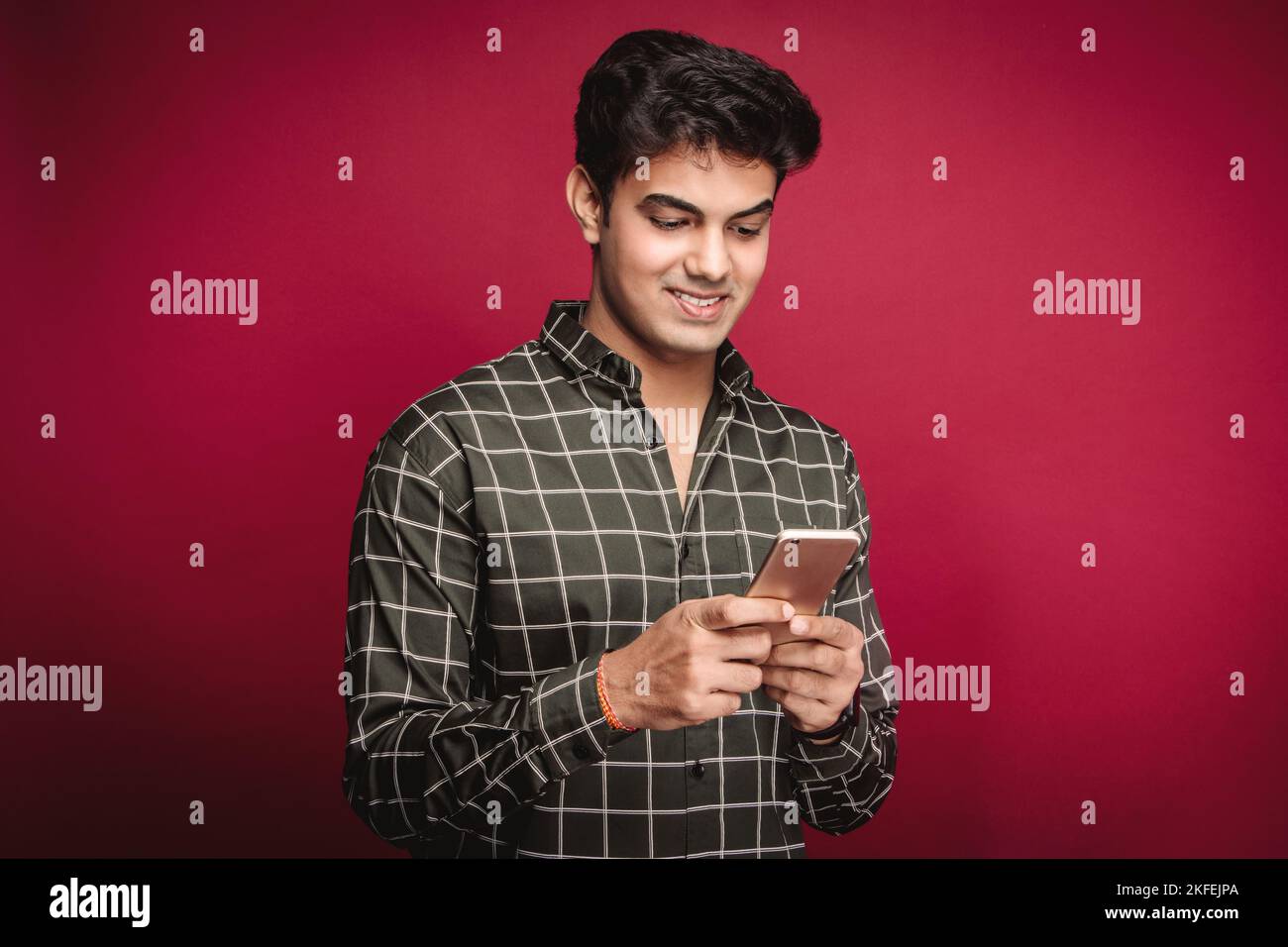 Smiling young Indian man in casual clothes using a mobile phone while