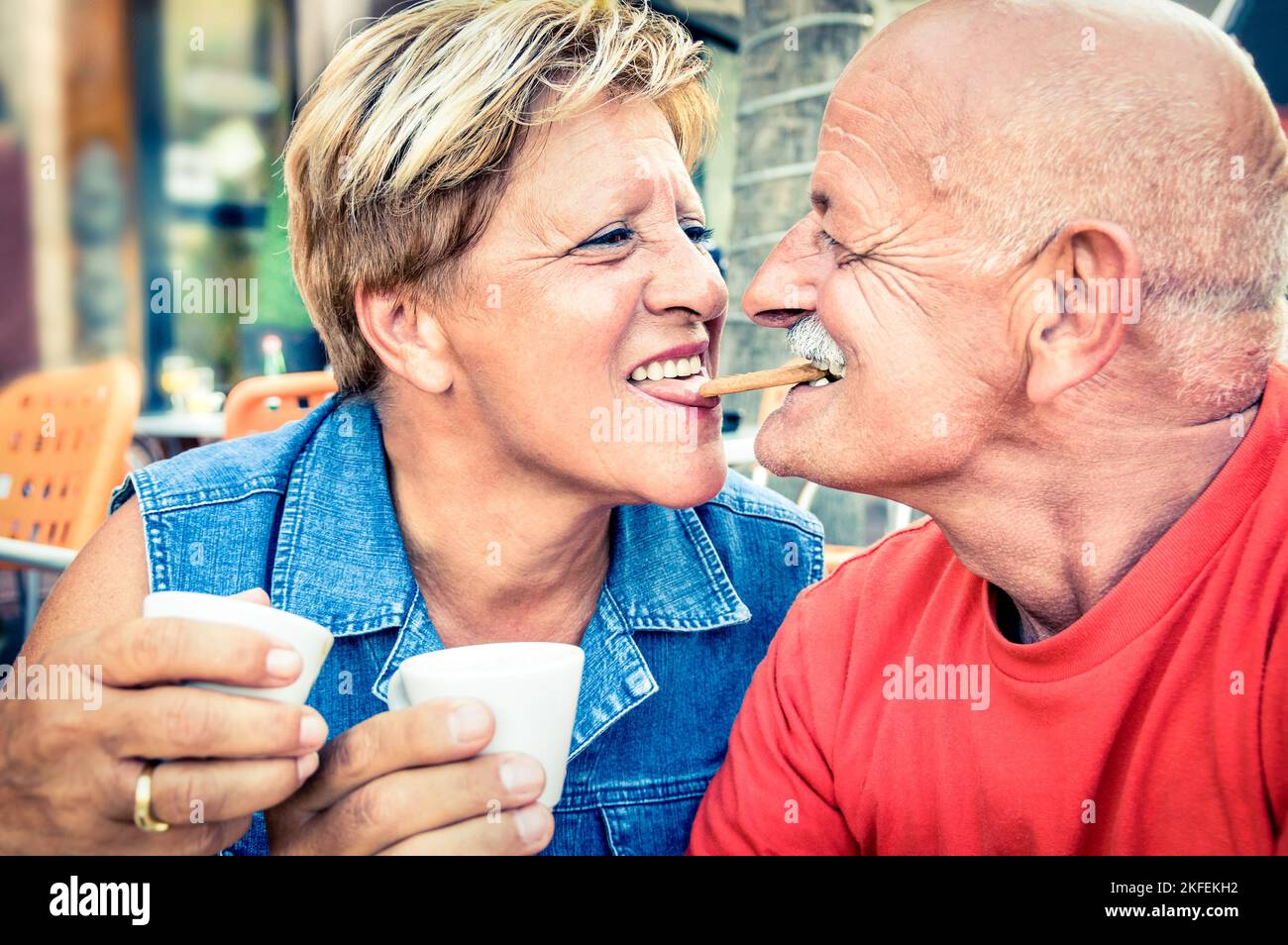 Happy playful senior couple in love tenderly enjoying a cup of coffee - Joyful elderly active lifestyle - Man having fun and smiling with her wife in Stock Photo