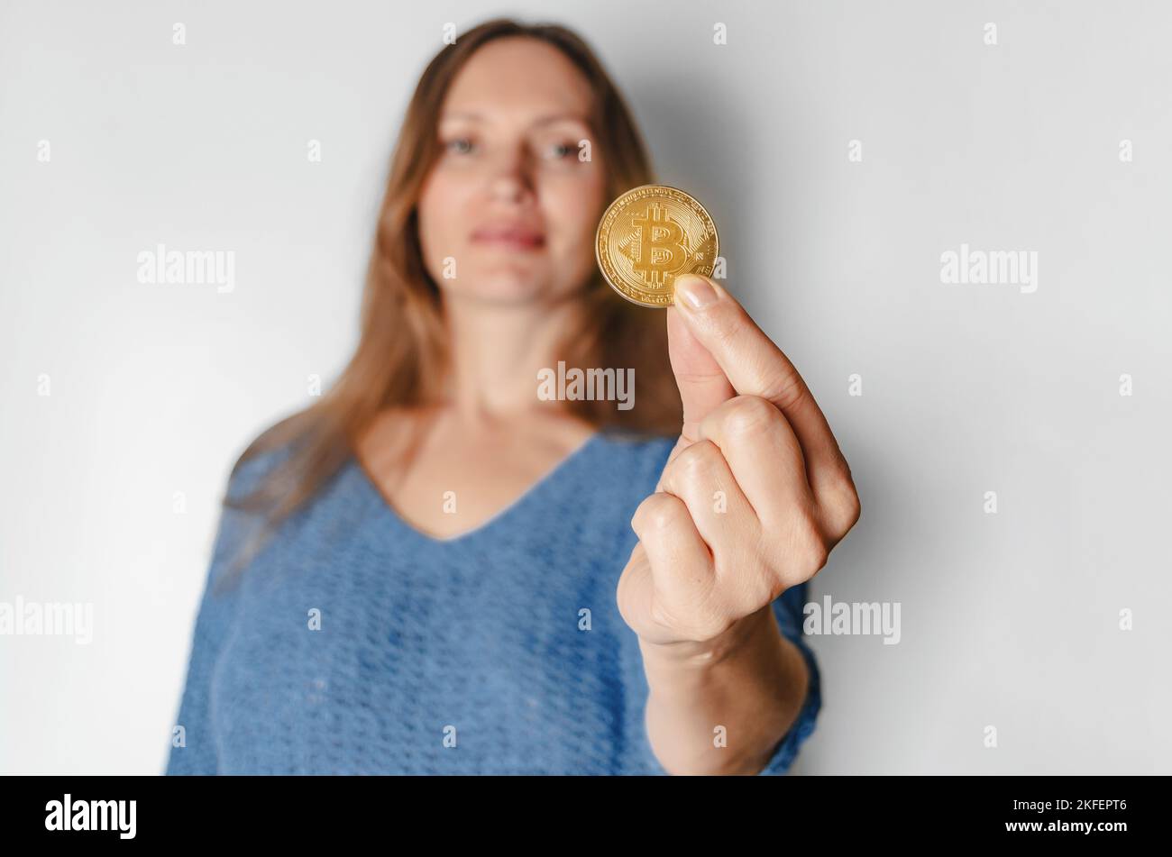 Portrait of woman in casual clothes looking at camera holding bitcoin, future currency, isolated on white background in studio. People lifestyle conce Stock Photo