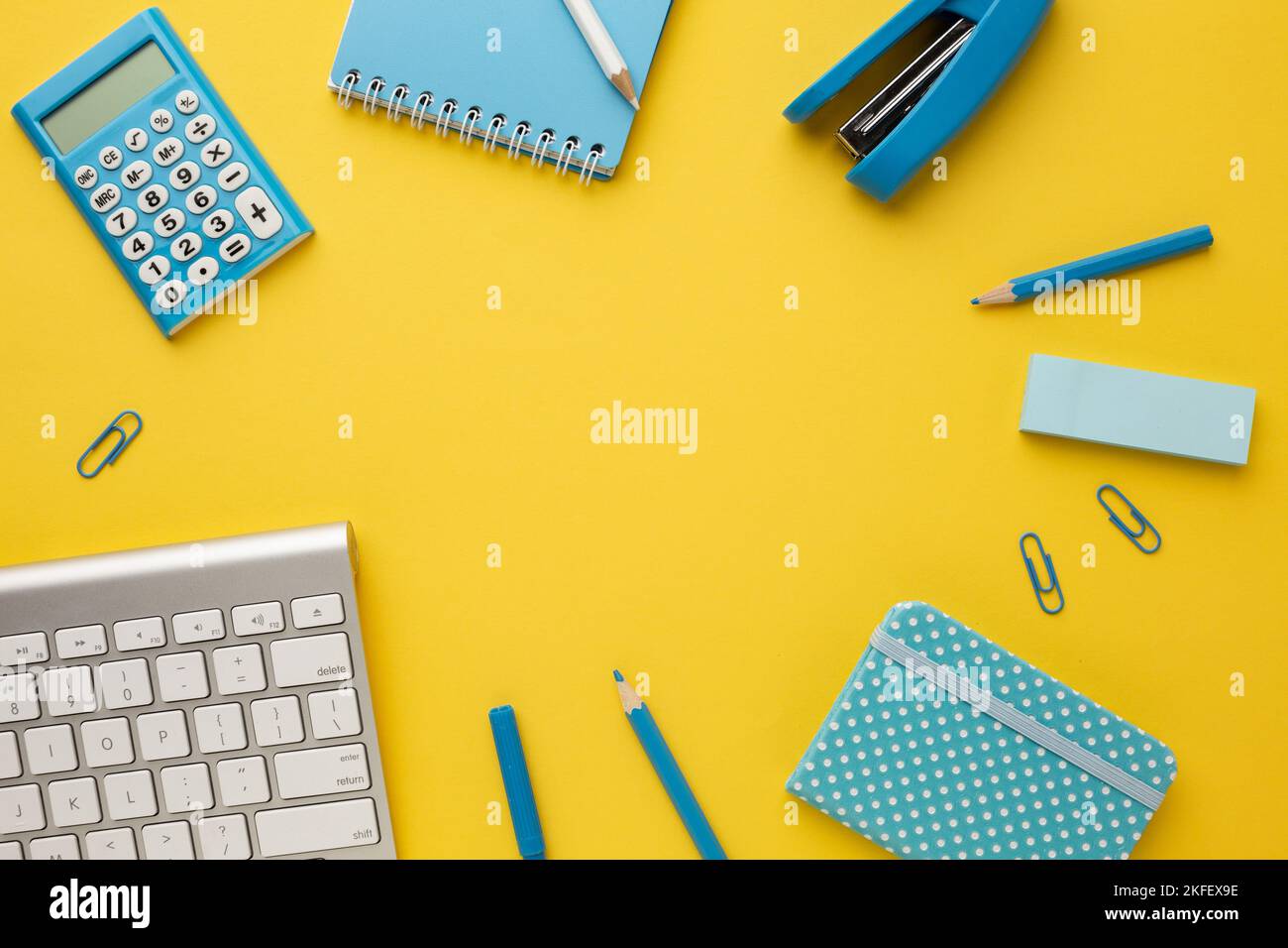Working yellow table with a keyboard, calculator, notebooks, eraser, pencil, felt-tip pen, stapler and paper clips. Top view with copy space. Stock Photo