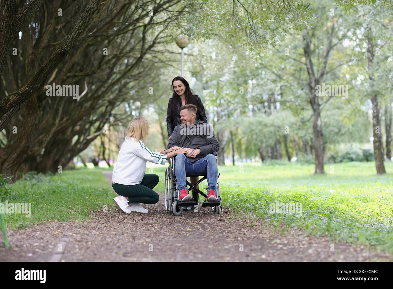 Smiling man in wheelchair and two women have fun in the park Stock ...