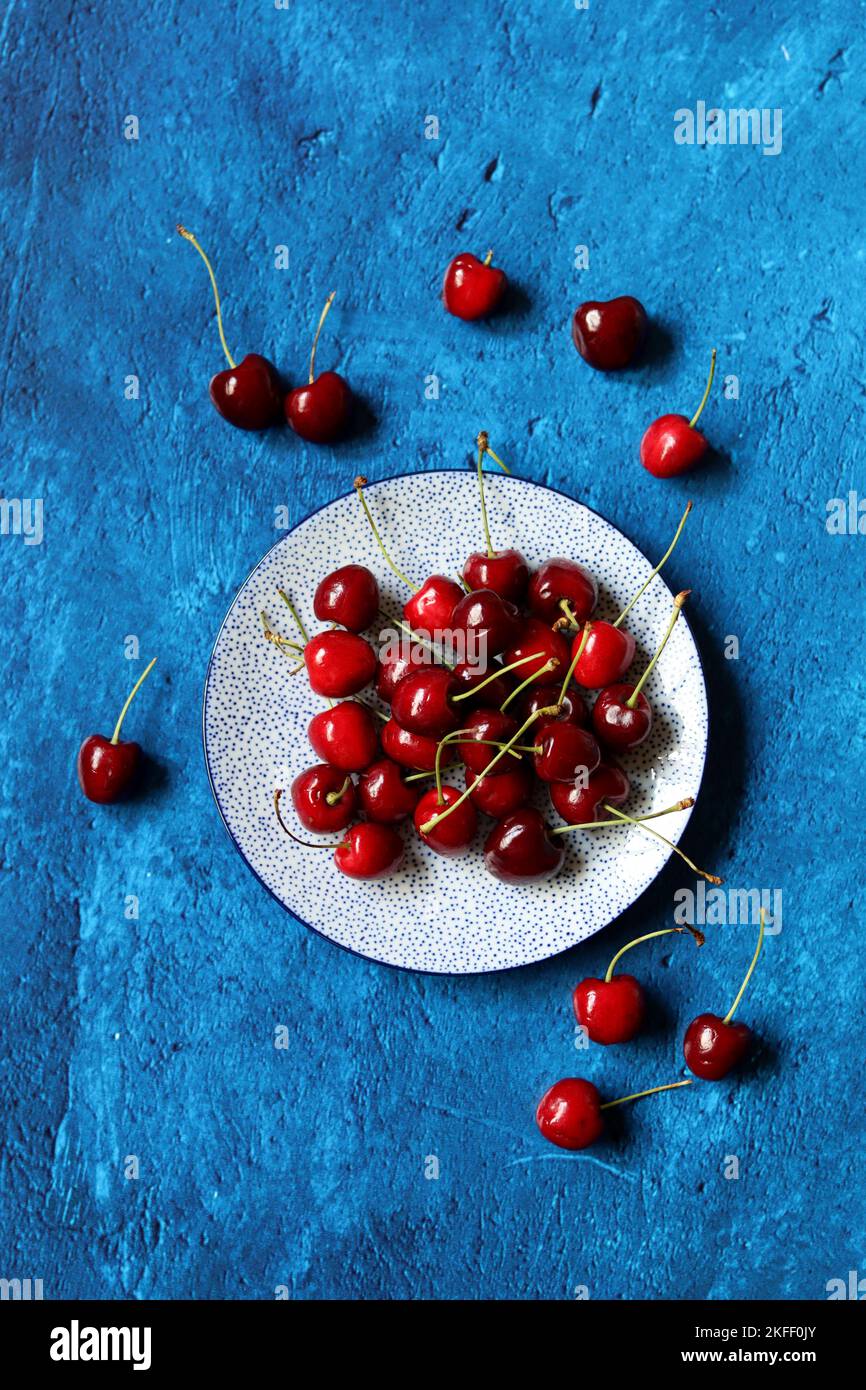 Sweet cherry on a plate. Top view photo of organic berries. Vibrant blue background with copy space. Summer still life with cherry. Stock Photo