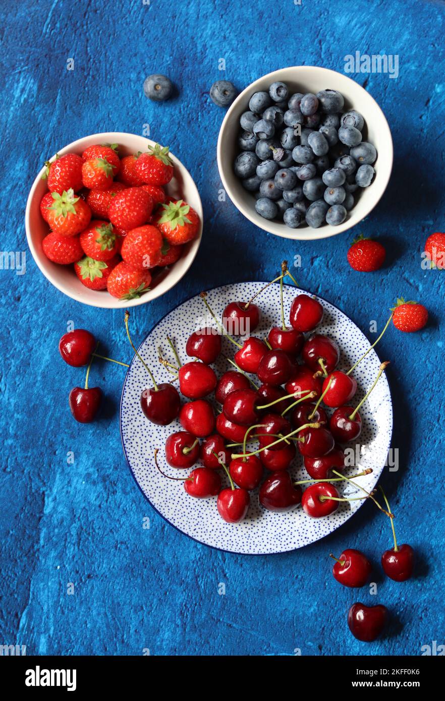 Summer still life with fresh berries on ceramic plates. Top view photo of organic cherry, blueberry and strawberry. Healthy eating concept. Stock Photo