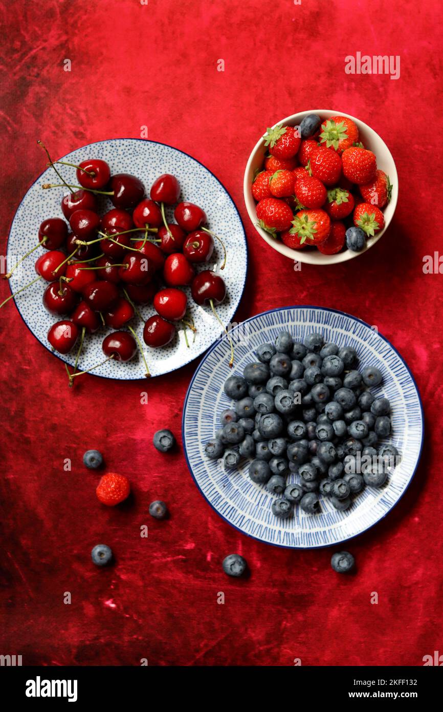 Summer still life with fresh berries on ceramic plates. Top view photo of organic cherry, blueberry and strawberry. Healthy eating concept. Stock Photo