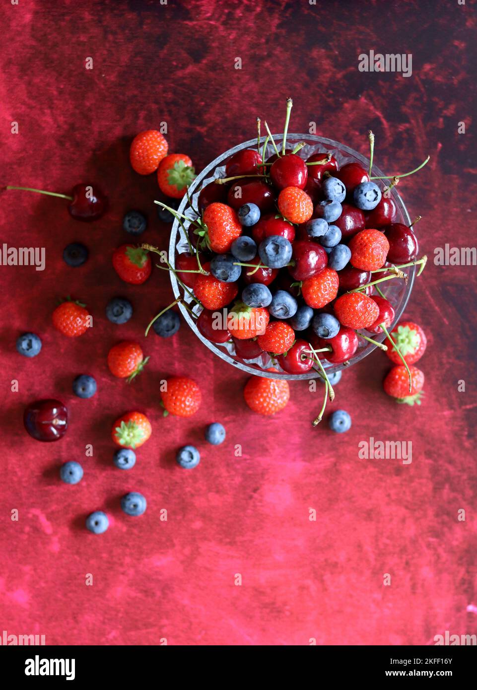 Top view photo of berries in a glass bowl. Vibrant colors of Summer. Red background with copy space. Natural antioxidants concept. Stock Photo