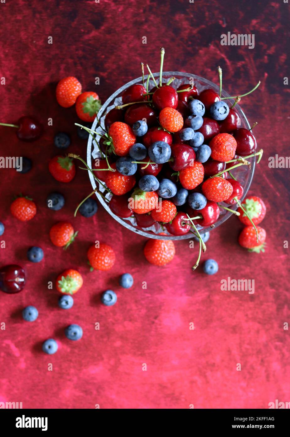Top view photo of berries in a glass bowl. Vibrant colors of Summer. Red background with copy space. Natural antioxidants concept. Stock Photo