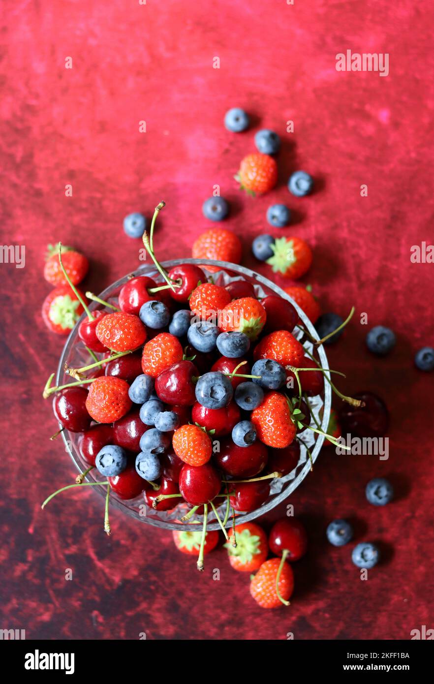 Top view photo of berries in a glass bowl. Vibrant colors of Summer. Red background with copy space. Natural antioxidants concept. Stock Photo