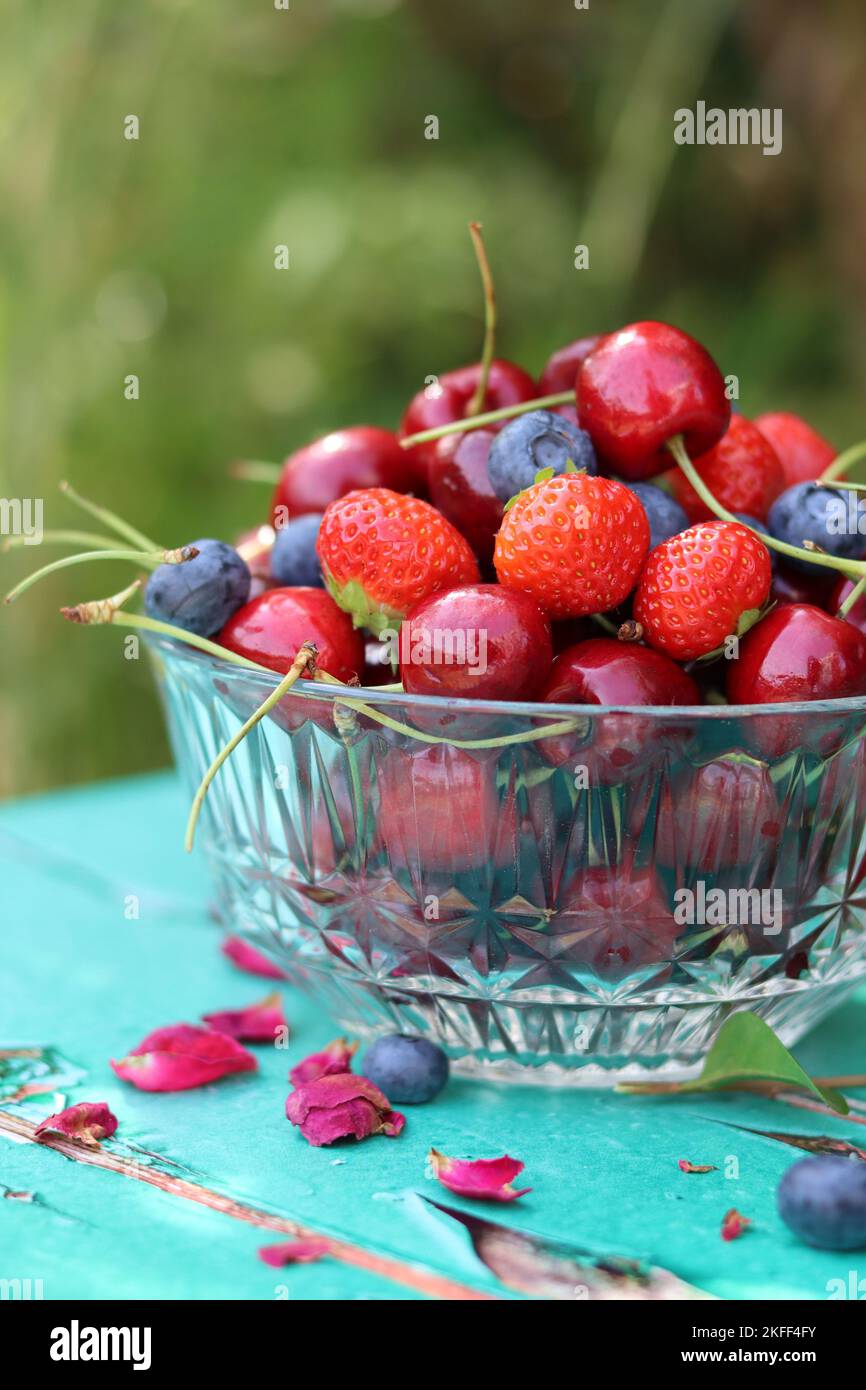 Glass bowl full of juicy organic berries. Summer still life with strawberry, sweet cherry, blueberry. Eating fresh concept. Stock Photo