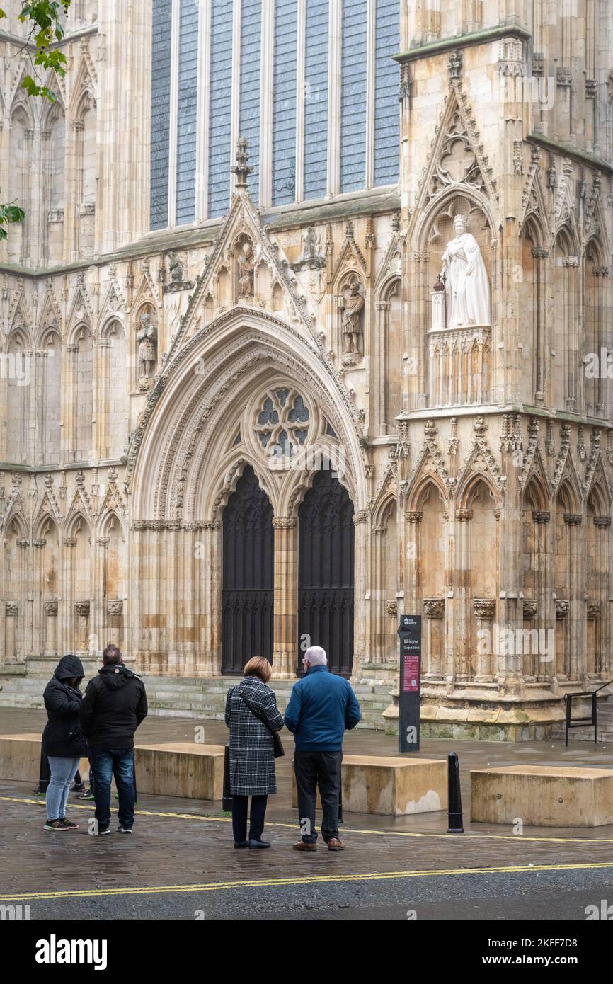 People looking up at the stone statue of Queen Elizabeth II on the
