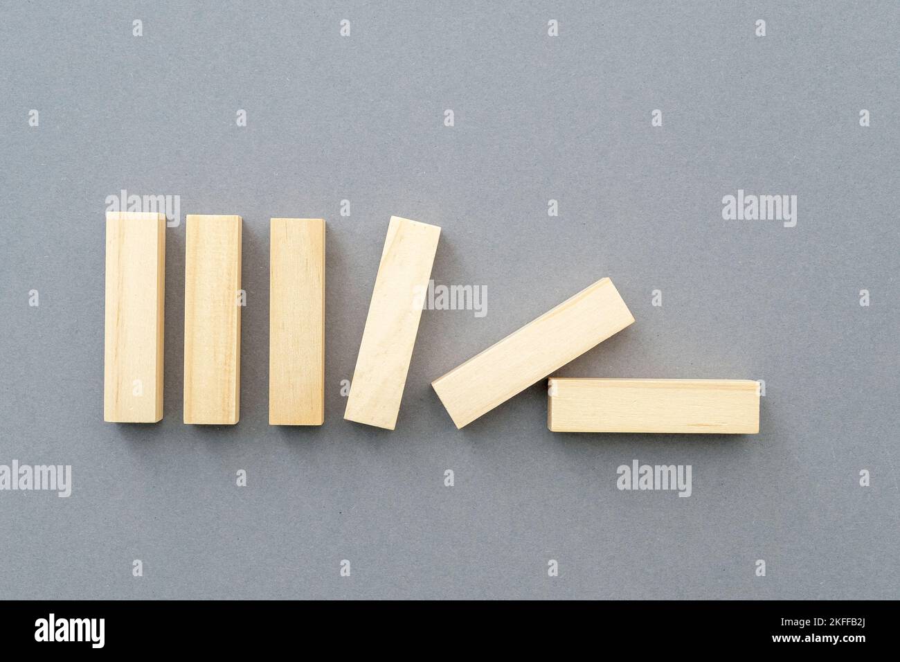 Row of falling vertical wooden shapes business concept picture about team building, leadership, supporting. Blank wooden figures on gray background. Stock Photo