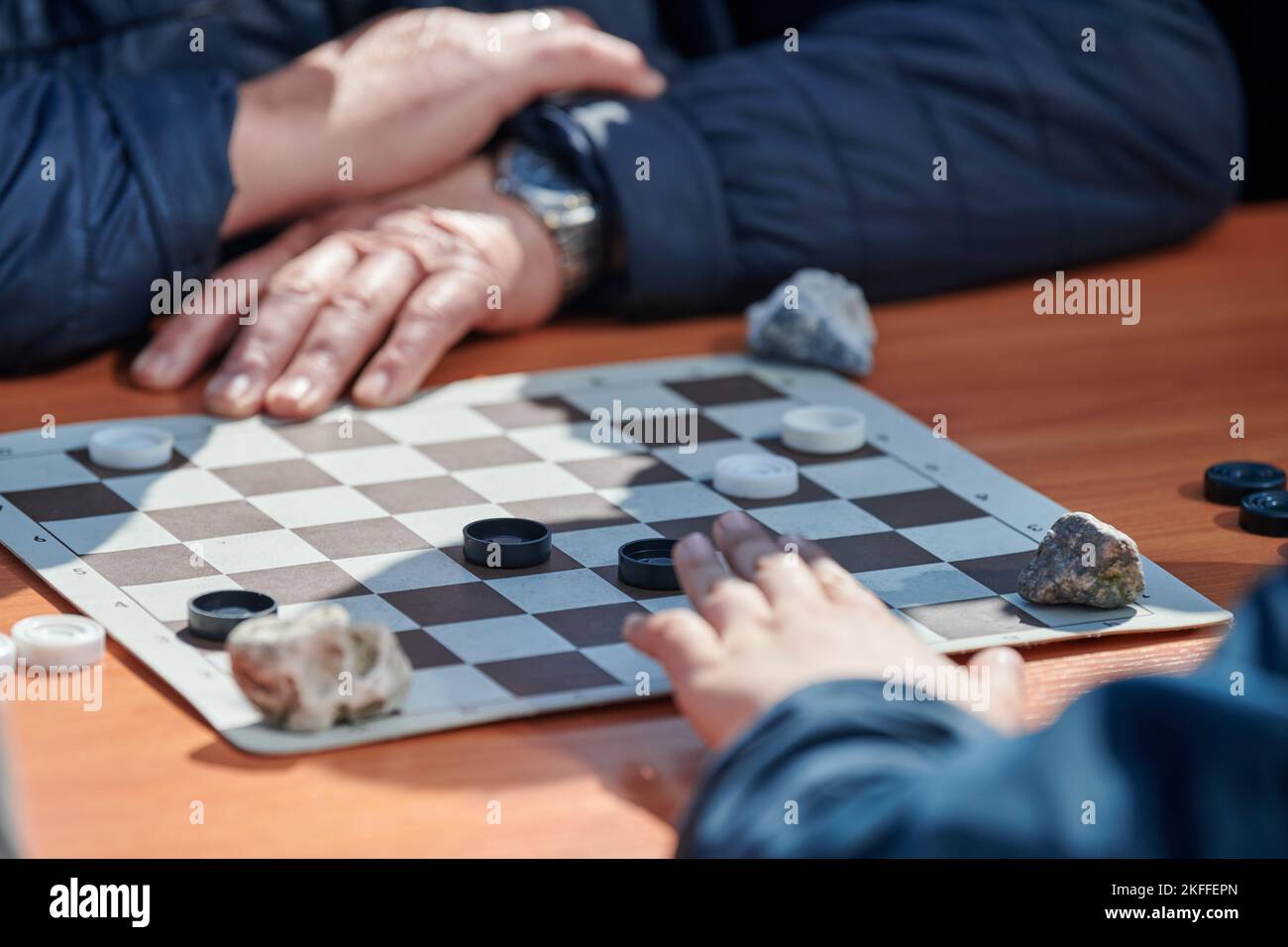 Outdoor checkers tournament on paper checkerboard on table, close up players hands. Outdoor