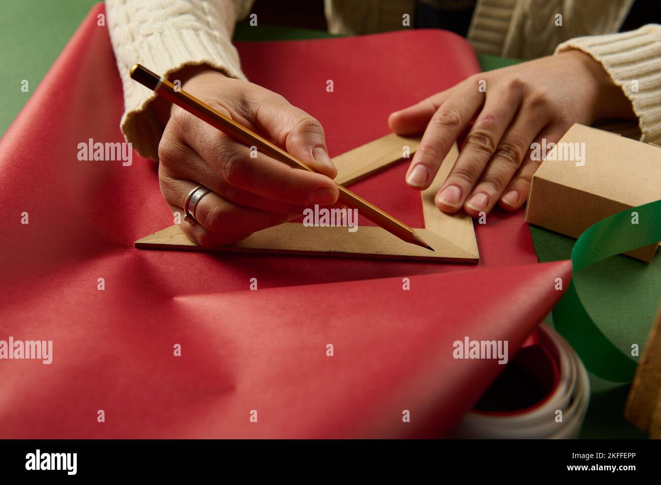 Woman's hands with wooden crayon and triangular ruler draw on wrapping