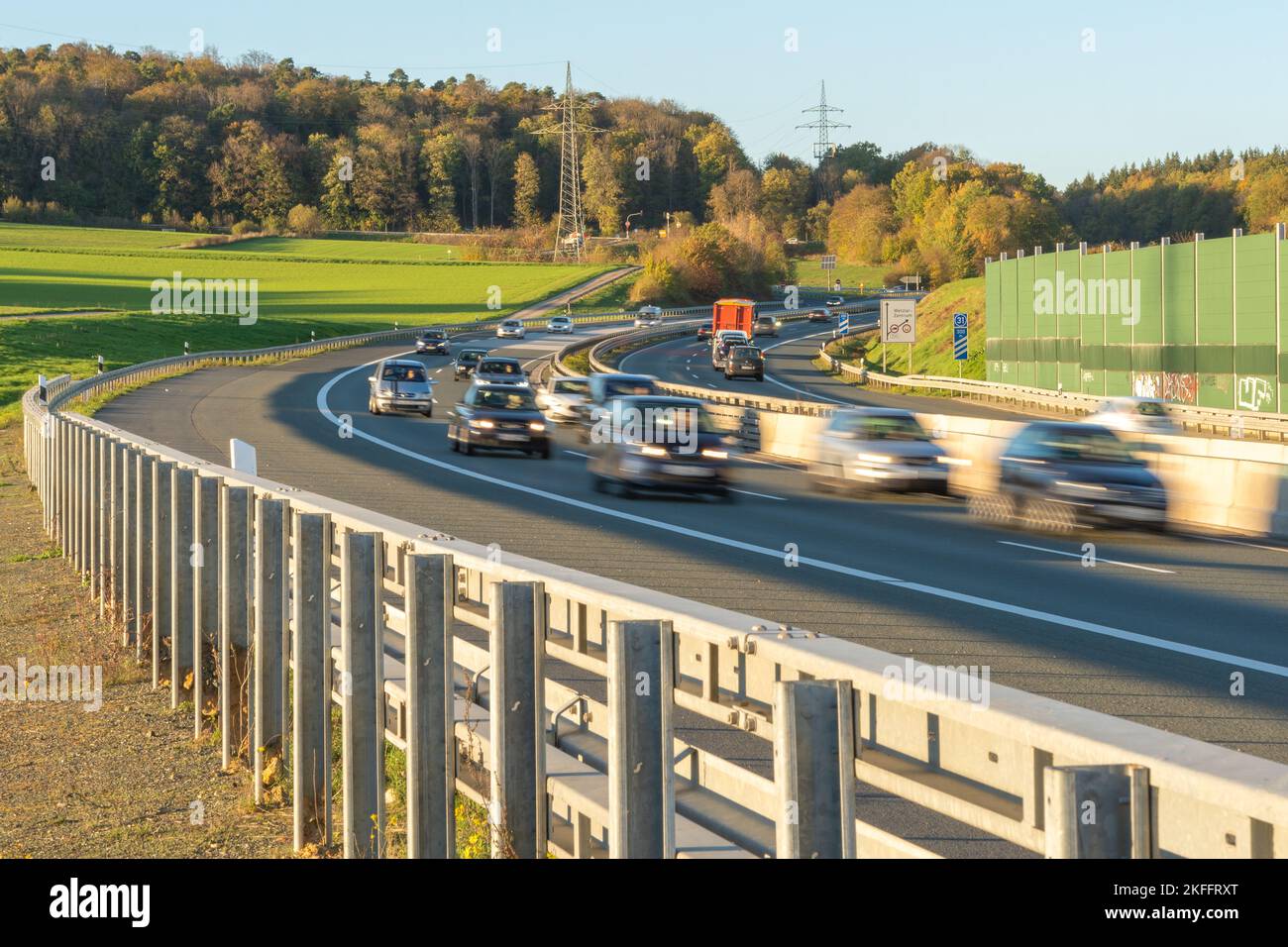 A German a45 autobahn highway full of moving cars surrounded by fields and tall trees during the daytime Stock Photo