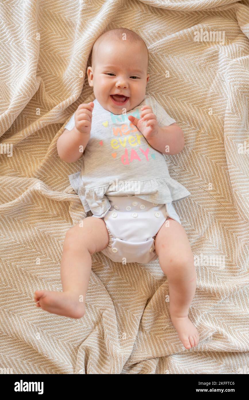 happy-baby-girl-lying-on-her-back-on-a-bed-she-is-wearing-a-modern