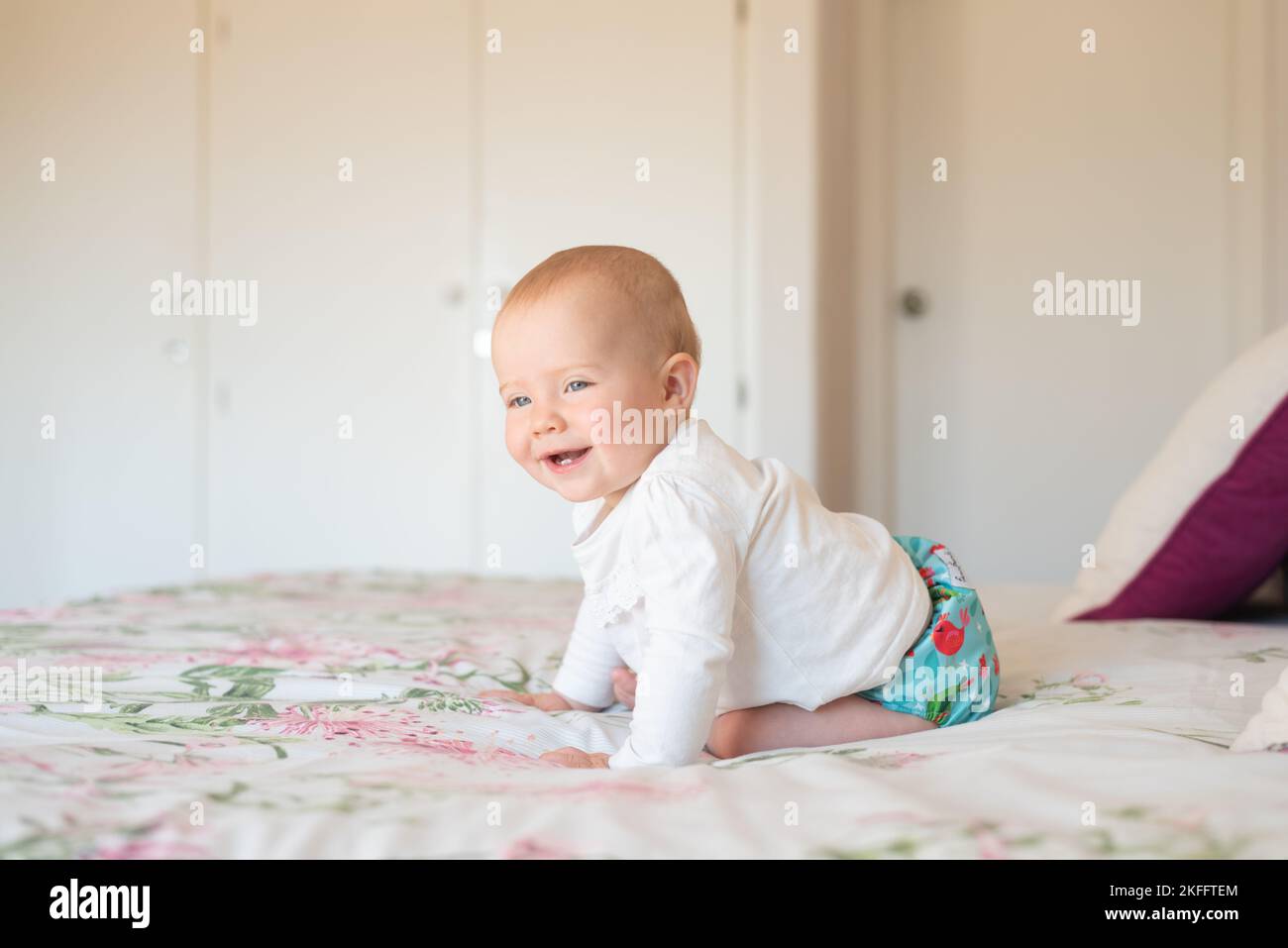 A happy baby girl learning how to sit. She is wearing a modern, reusable cloth diaper Stock