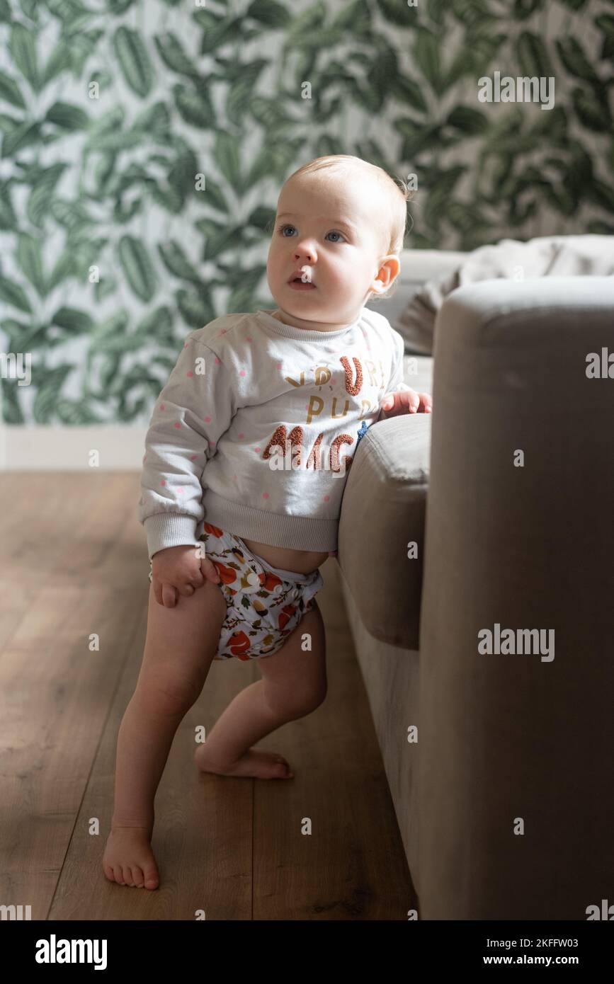 A baby girl learning how to stand up. She is wearing a modern, reusable