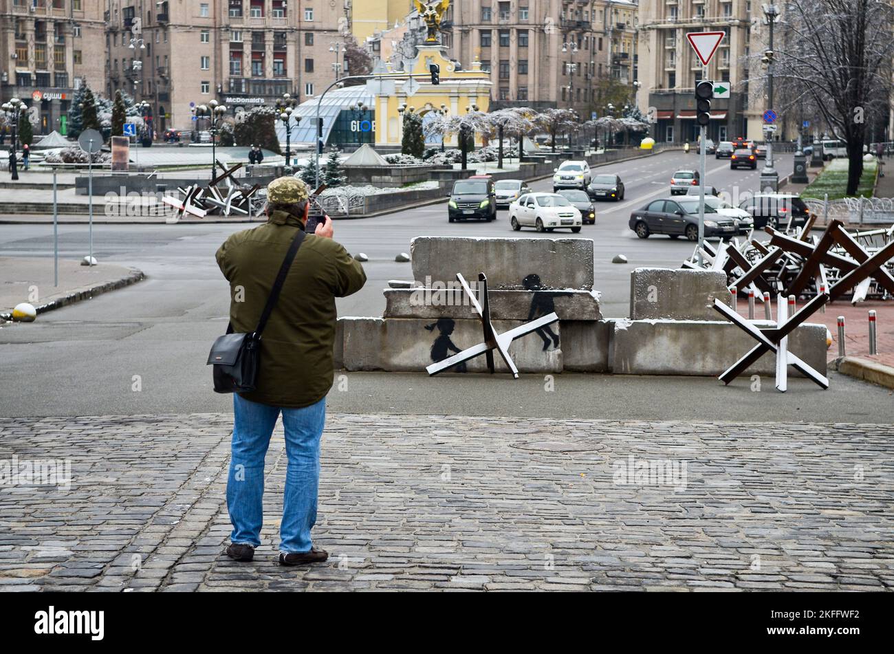 KYIV, UKRAINE - NOVEMBER 17, 2022 - A man takes a picture of the mural by England-based street artist Banksy which transforms an anti-tank obstacle (C Stock Photo