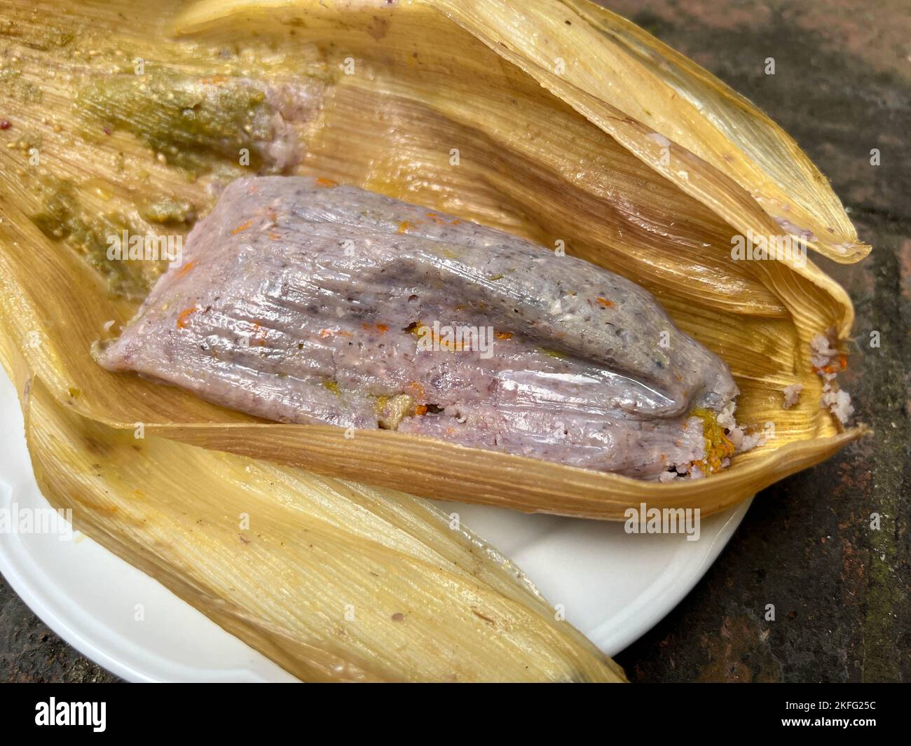 Tamale made from blue corn with squash blossoms wrapped in a corn husk ...