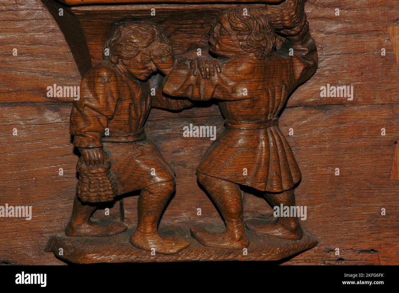 “One attacks while the other soothes”: old Dutch proverb or saying illustrated by sculpted misericord beneath choir stall seat in the Oude Kerk (Old Church) in Ouderkerksplein, Amsterdam, Netherlands.  Two men fight while holding baskets - but one calms his opponent’s brow. Stock Photo