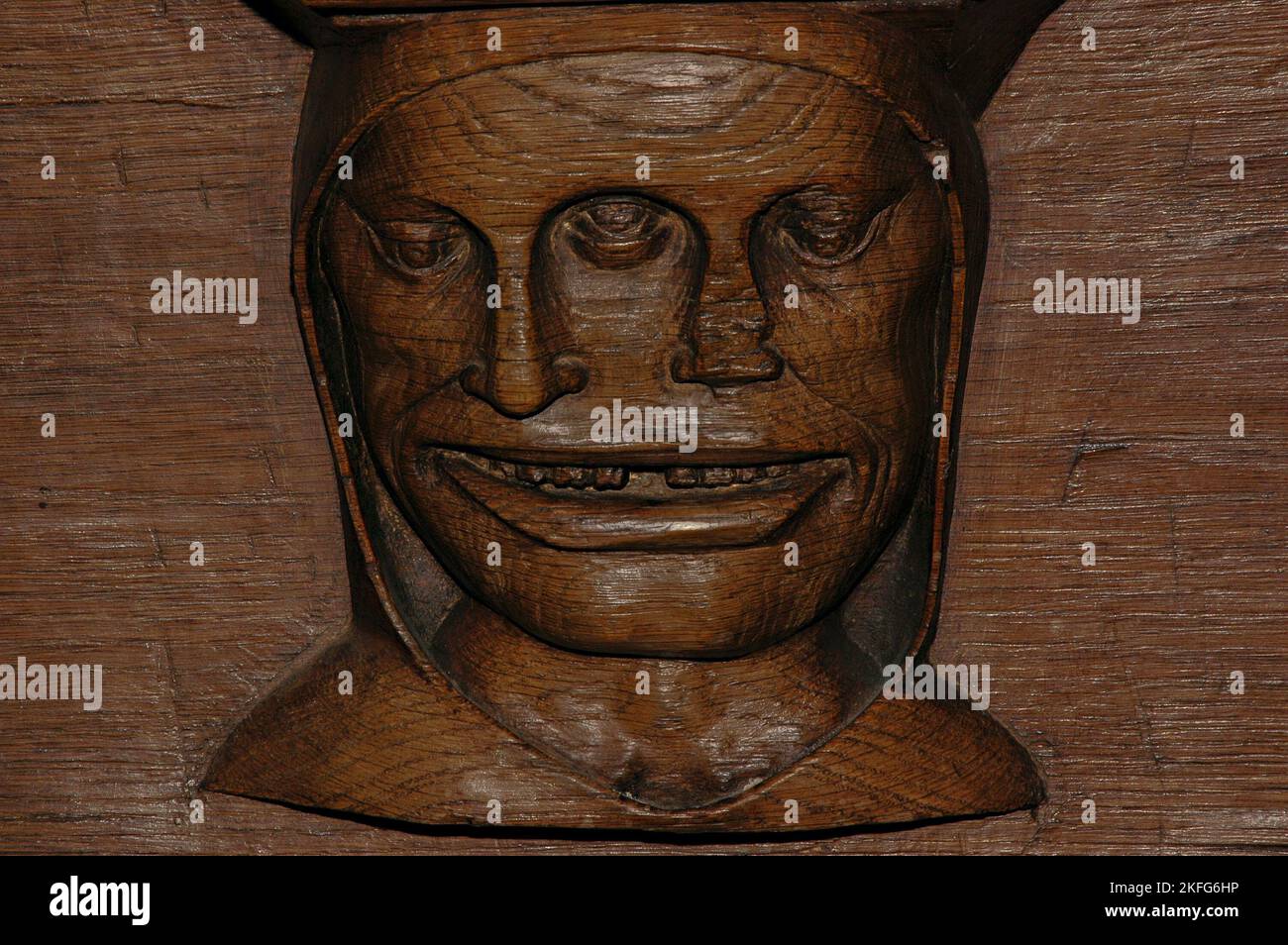 Hooded face with three eyes and two noses, believed to be a comment on how drunken people tend to agree with each other about everything.  Late 1400s sculpted misericord beneath choir stall seat in the Oude Kerk (Old Church) in Ouderkerksplein, Amsterdam, Netherlands. Stock Photo