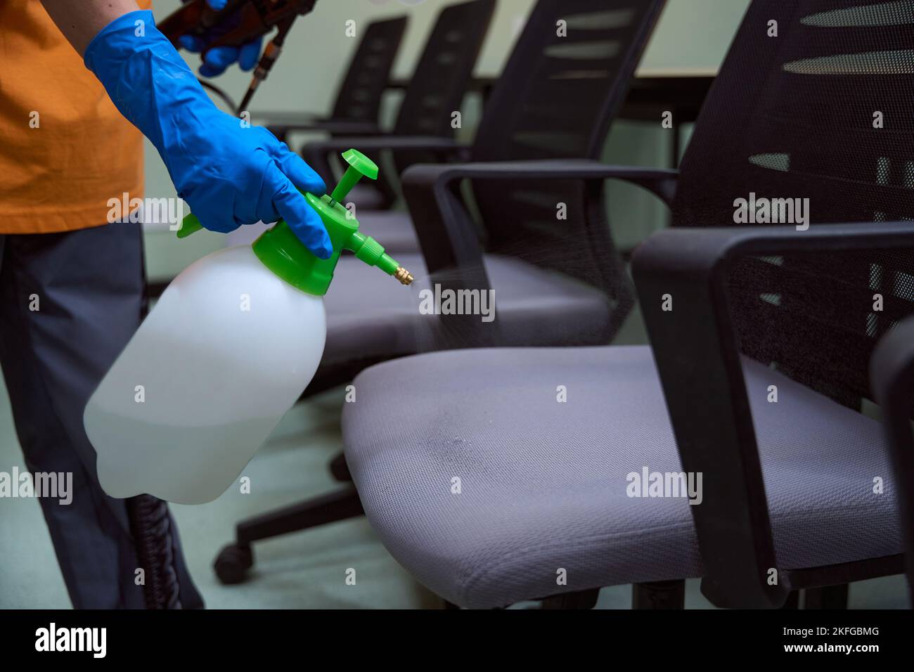 Well-trained janitor with sanitizer spray following room sanitation protocols Stock Photo