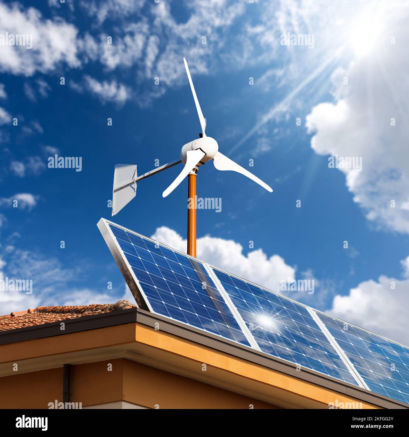 Solar panels and a small wind turbine on the top of a roof of a house ...