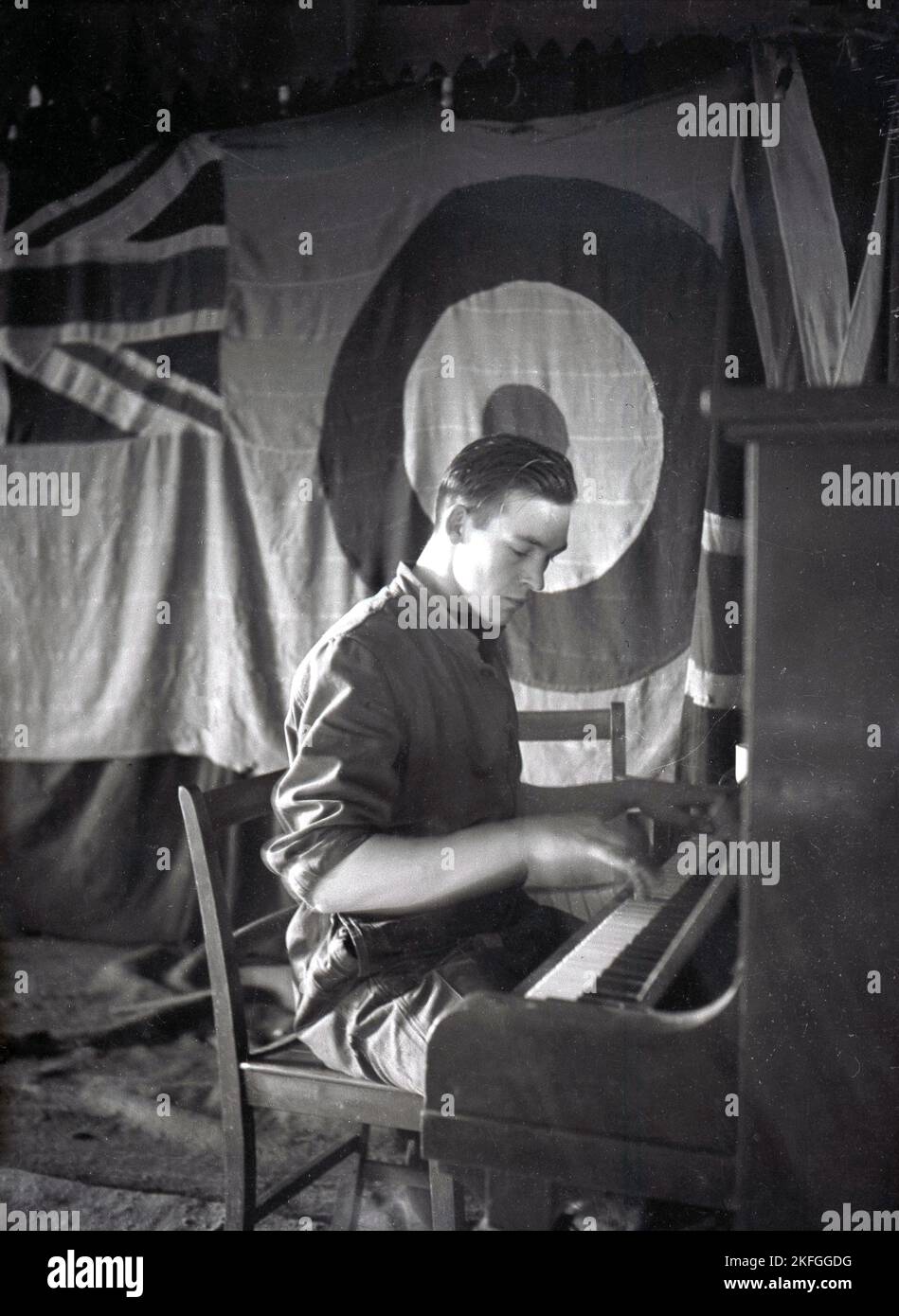 1948, historical, a British airman sitting playing the piano at Longford Camp, RAF Ternhiill, Market Drayton, Shropshire, England, UK. A hanging cloth backdrop on the stage has a union jack logo and the RAF roundel, first introduced with the Royal Flying Corps in WW1. Stock Photo
