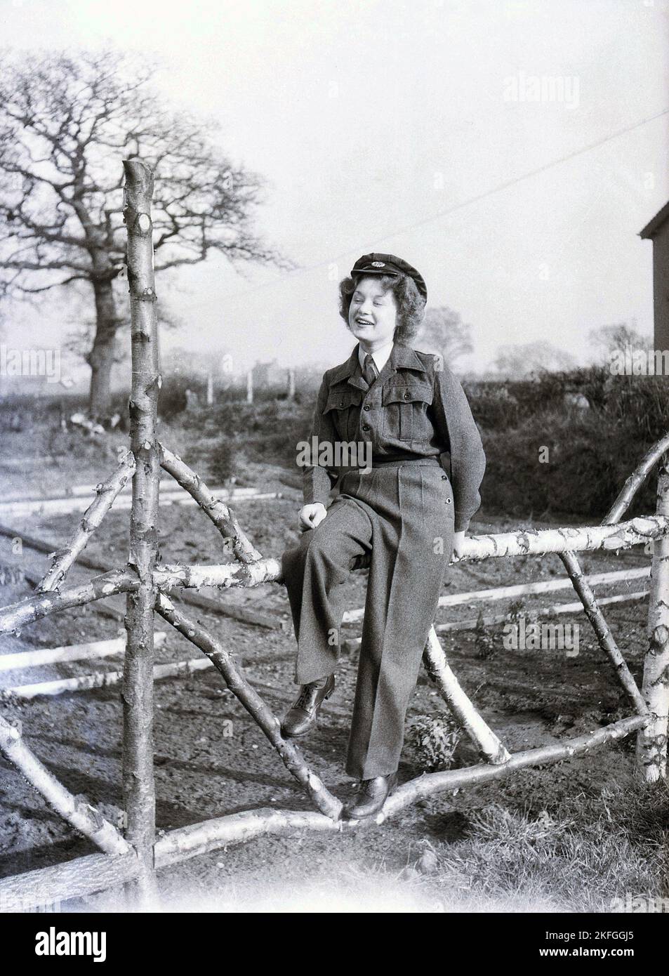 1940s, historical, posing for a photo on a fence outside Longford Camp, at RAF Ternhill near Market Drayton, Shropshire, England, UK, a young female WAAF in a collar and tie, woollen cloth tunic and trousers and hat. The Women's Auxillary Air Force (WAAF) was formed in June 1939, with intital recruits being between 18-43 years old. Stock Photo