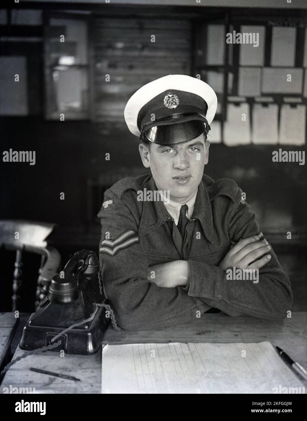 1948, historical, an RAF airman, a corporal, in his uniform and hat sitting at a desk with a telephone of the era and paper pad at the Longford Camp, at RAF Ternhill, near Market Drayton, Shropshire, England, UK. An RAF badge is on his hat. Stock Photo