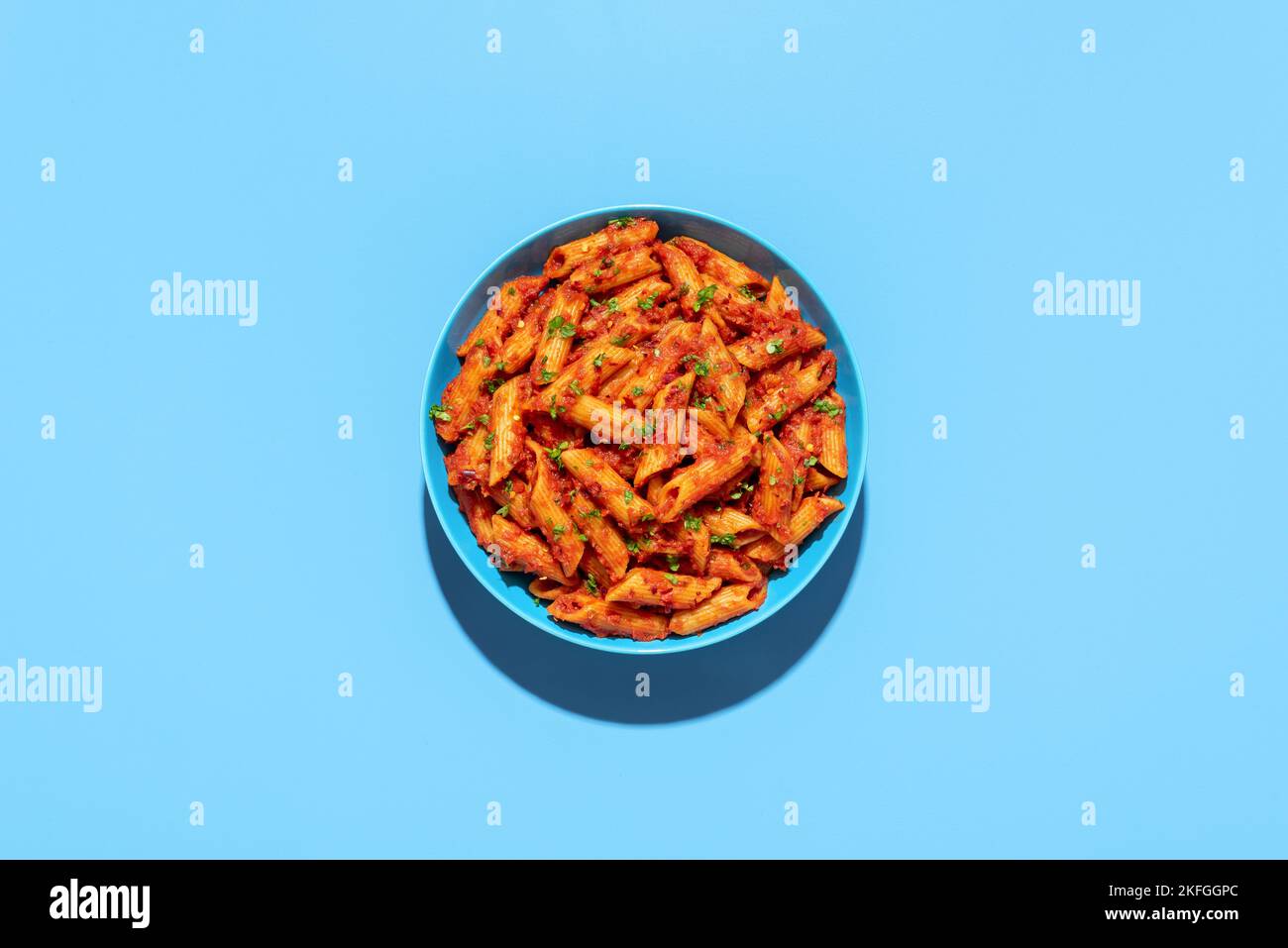 Top view with a portion of penne alla arrabbiata minimalist on a blue table. Italian dish, penne with spicy tomato sauce. Stock Photo