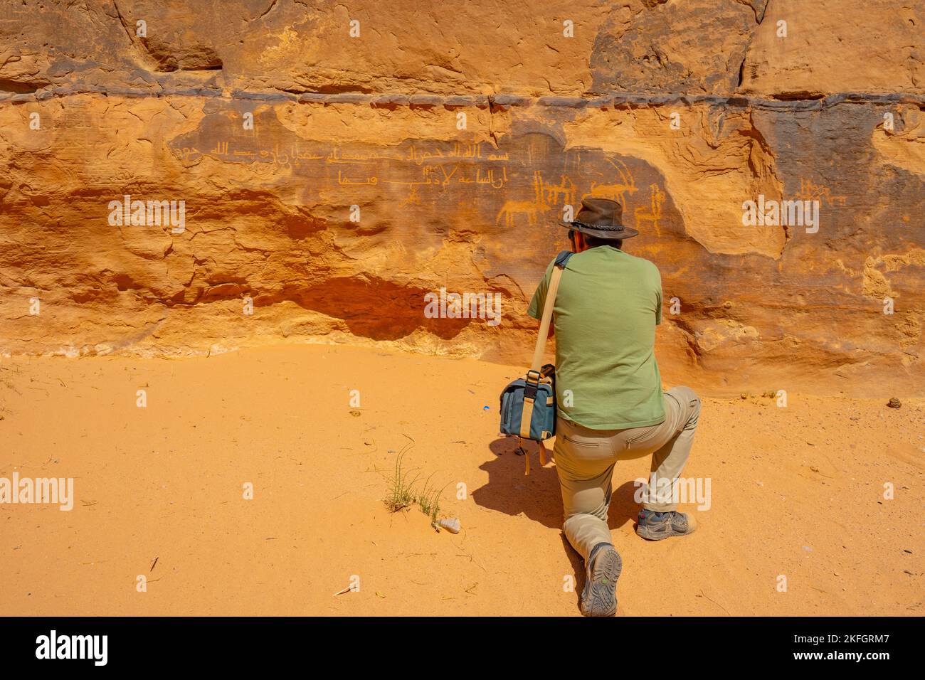 Tourist photographing ancient rock art on a cliff in Wadi Rum Jordan, Stock Photo