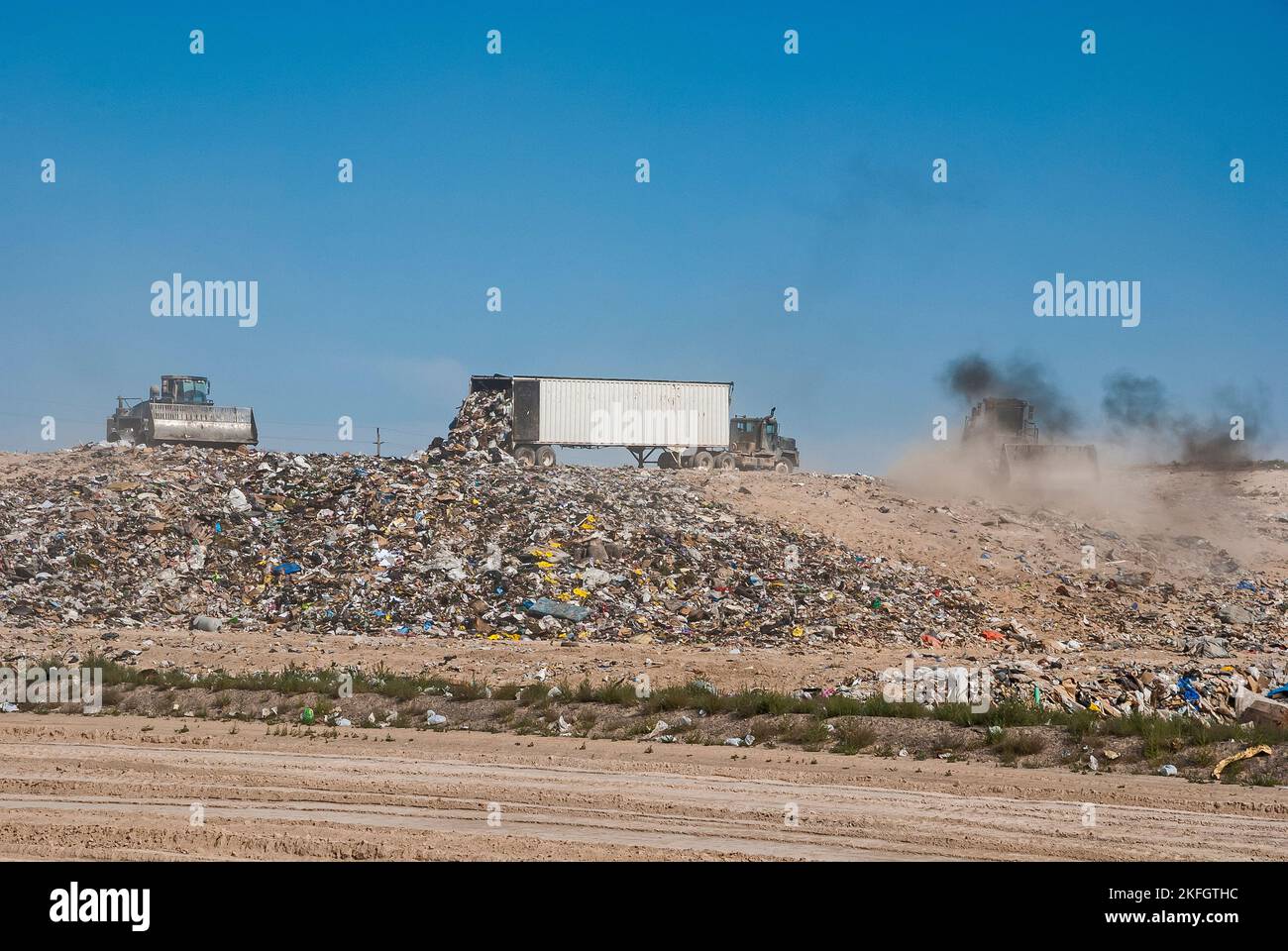Two soil compactors and a semi tractortrailer on a hill in an active landfill. One of the soil