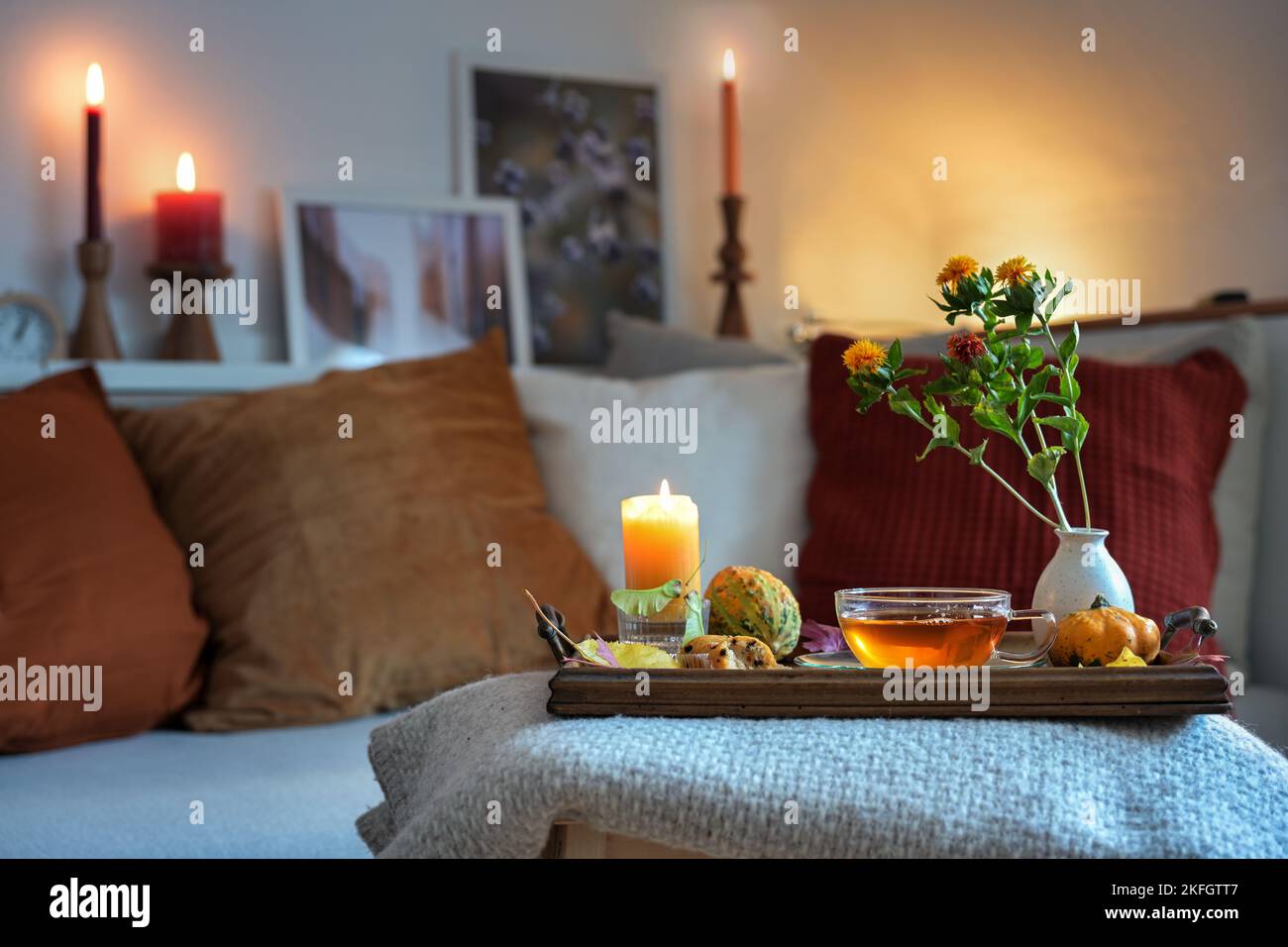 Relaxation with tea, candles and autumn decoration on a tablet in front of the couch in the cozy living room, copy space, selected focus, narrow depth Stock Photo